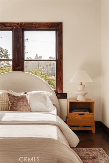 Bedroom with a white bed, rounded headboard, and dark wood-framed window.