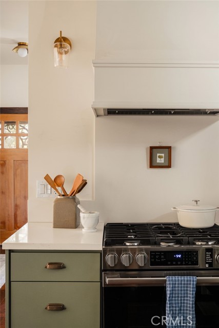 Kitchen with sage-green drawers, a stainless-steel gas range, and a white range hood.