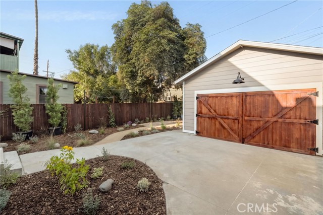 Detached garage with wooden double doors, a broad concrete driveway, and landscaped planting beds.