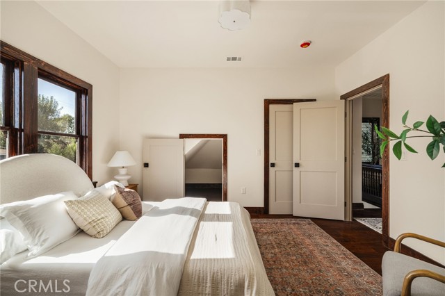 Bedroom with a white bed, dark wood window frames, and an open balcony doorway.