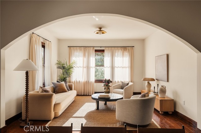 Living room with a broad arched opening, cream seating, and sunlight through sheer curtains.