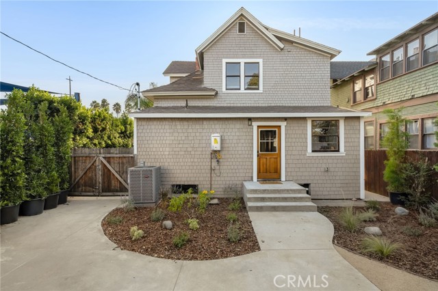 Gray shingle-sided two-story house with a wood entry door, concrete walk, and front landscaping.