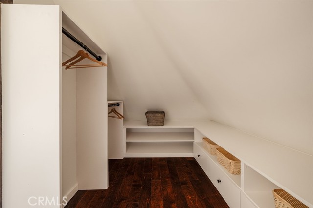 Walk-in closet with a sloped ceiling, dark hardwood flooring, and built-in white shelving.