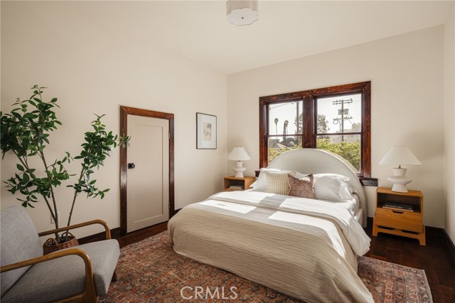 Bedroom with a white bed, patterned rug, and dark wood-framed windows.