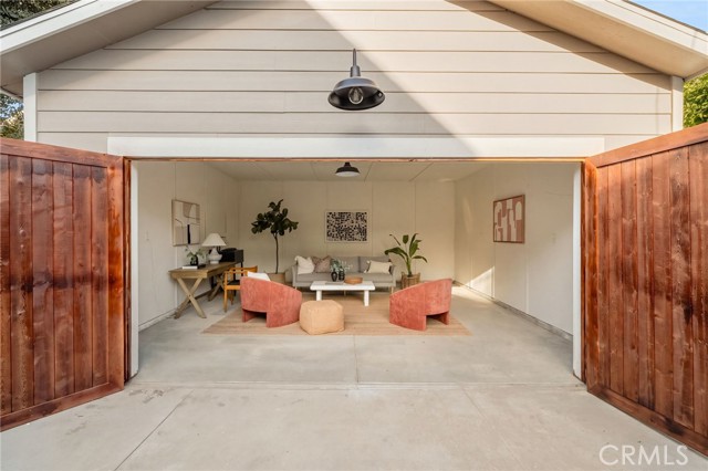 Staged lounge with coral chairs inside an open garage with wooden doors.
