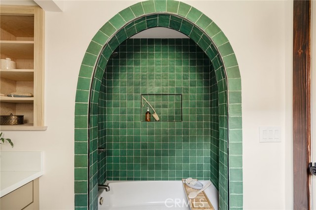 Bathroom bathtub in an arched alcove lined with glossy green tile.