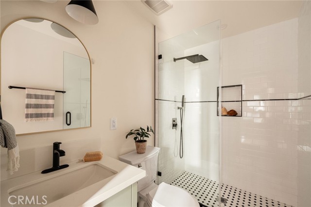 Bathroom with a glass-enclosed tiled shower, patterned floor, white vanity, and arched mirror.