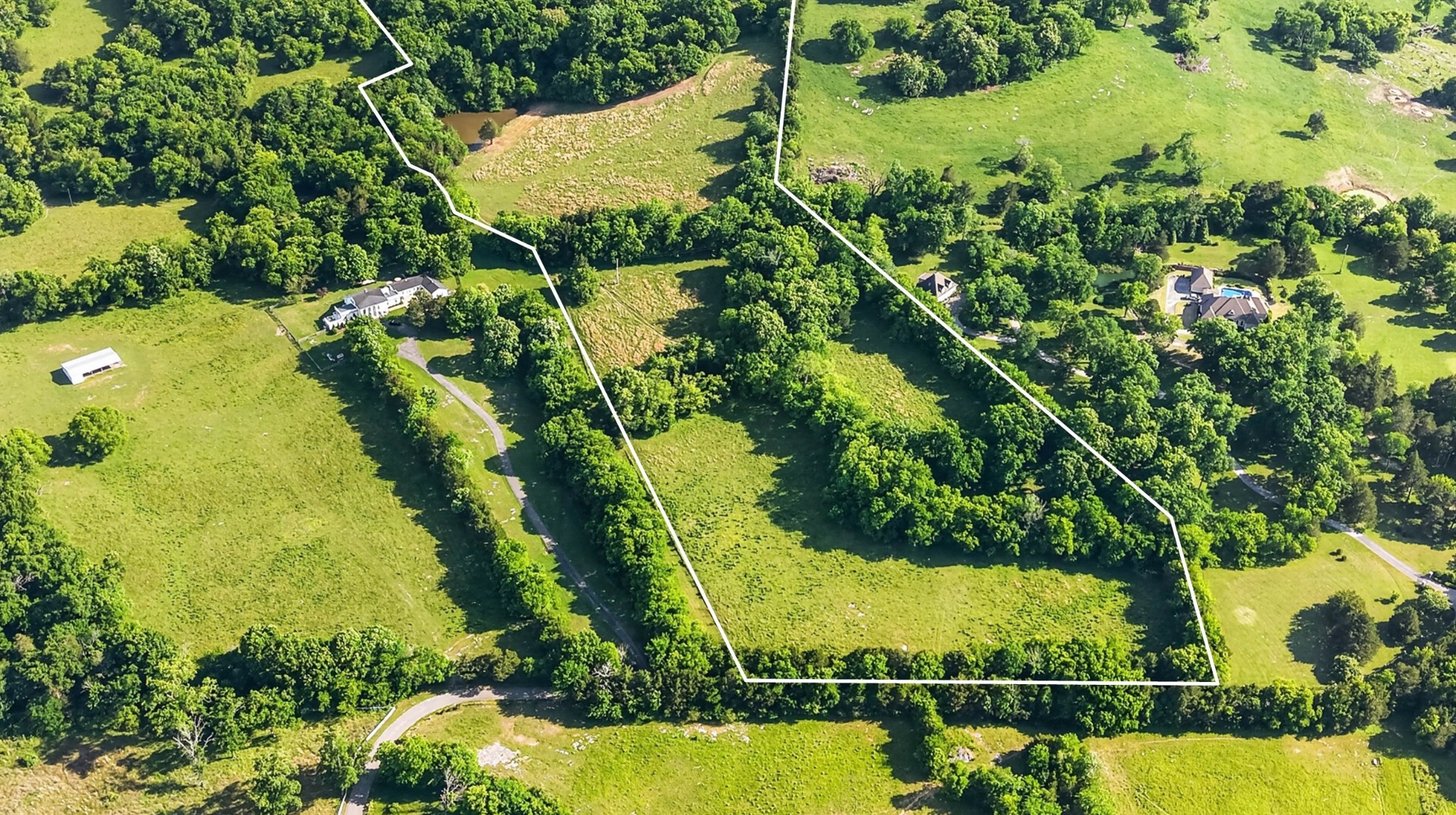 Aerial view of a wooded rural tract outlined in white amid open pasture and nearby homes.