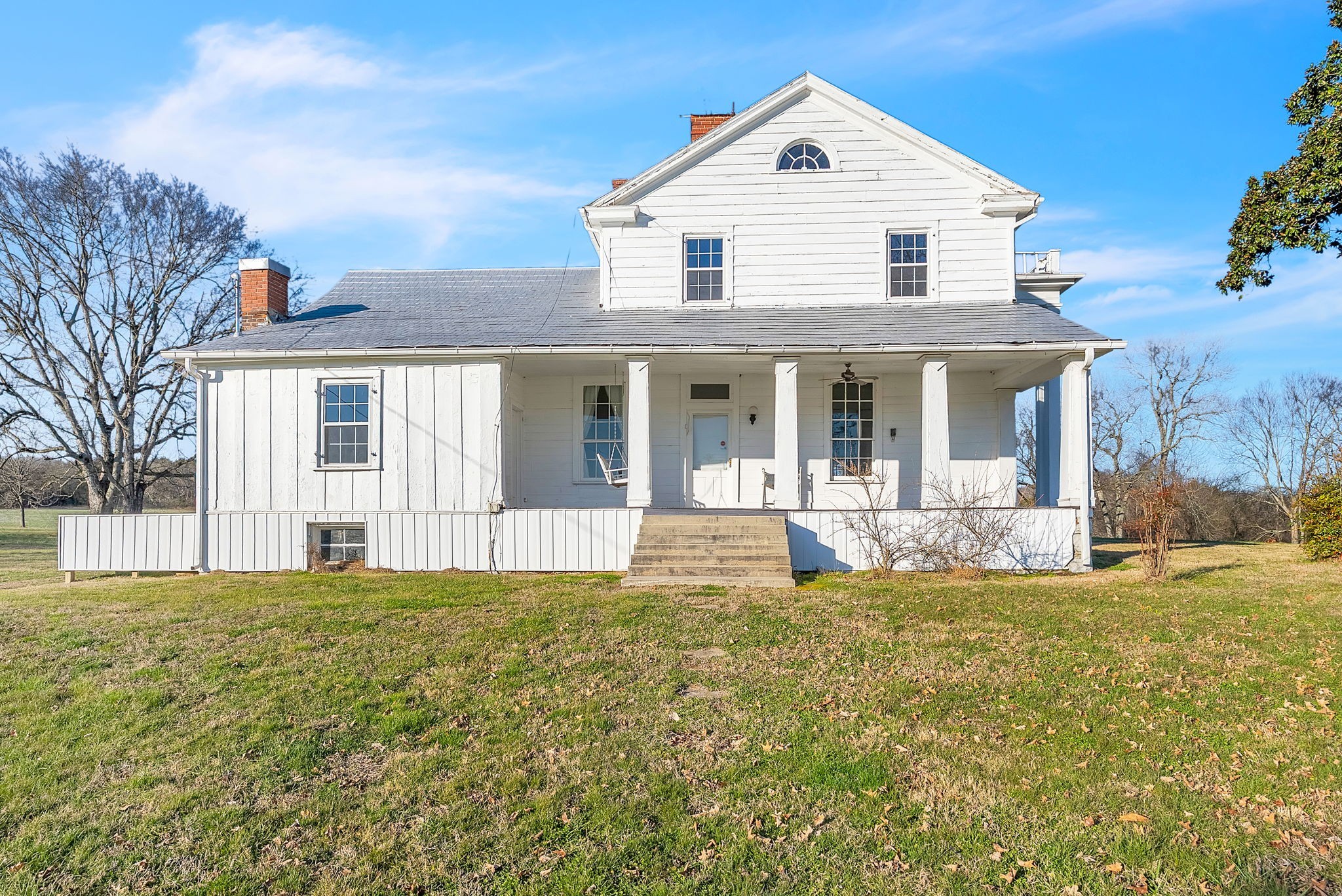 White two-story farmhouse with a broad columned porch and front steps on a grassy lawn.