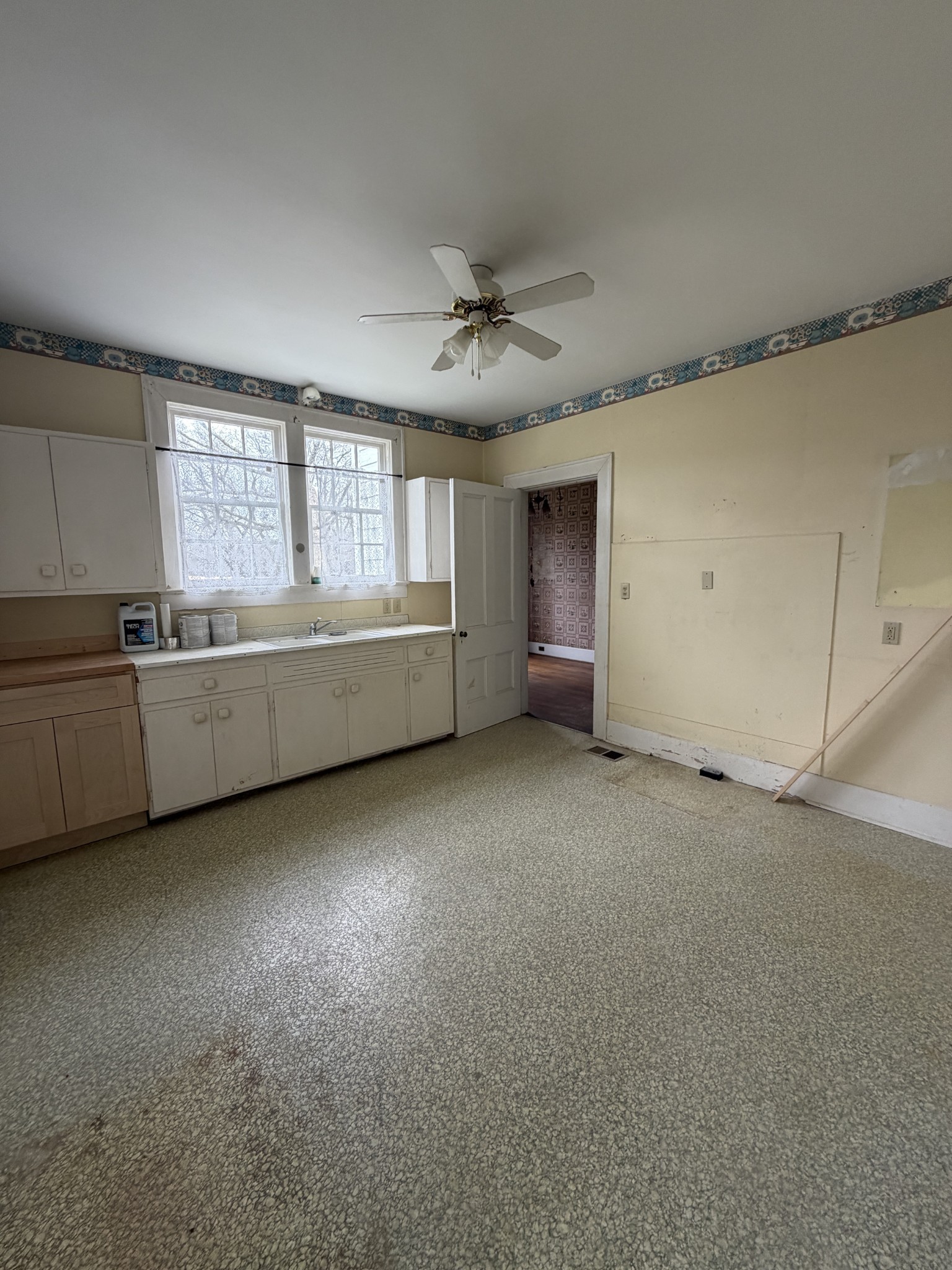 Vacant kitchen with built-in cabinets, double windows, patterned wall border, and ceiling fan.