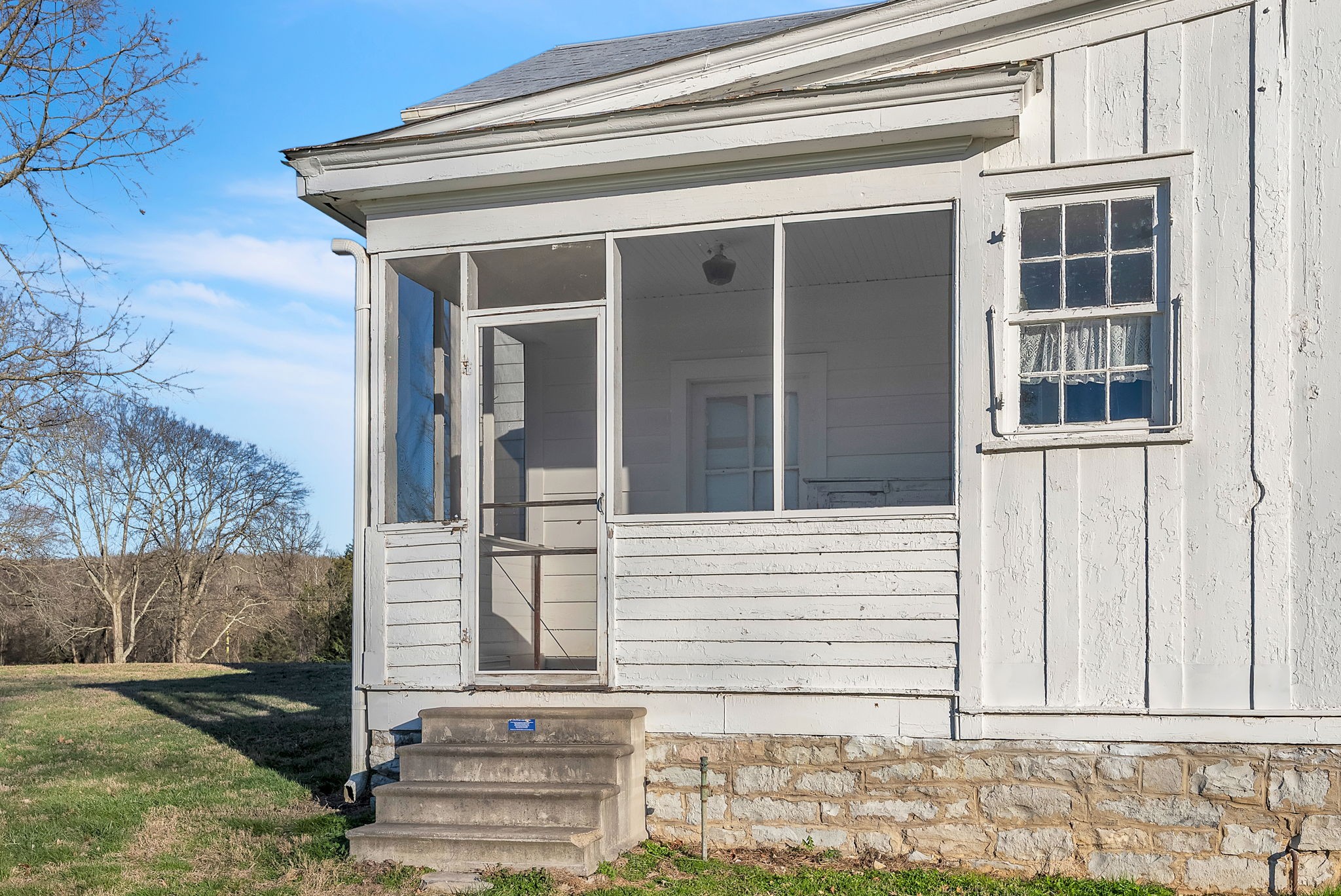 White house with a screened porch, concrete steps, and stone foundation.