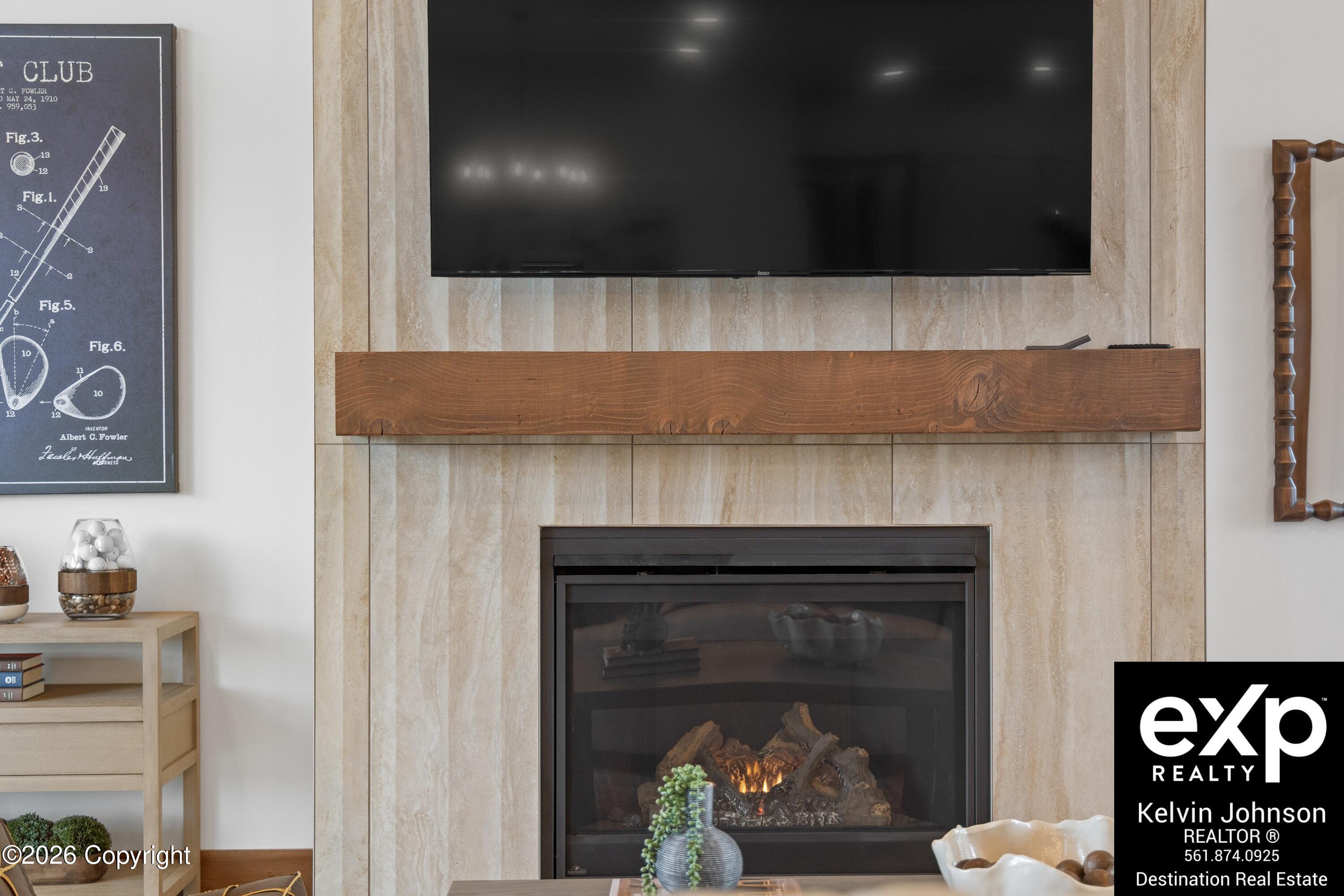 Living room fireplace with a beige stone surround, thick wood mantel, and television above.