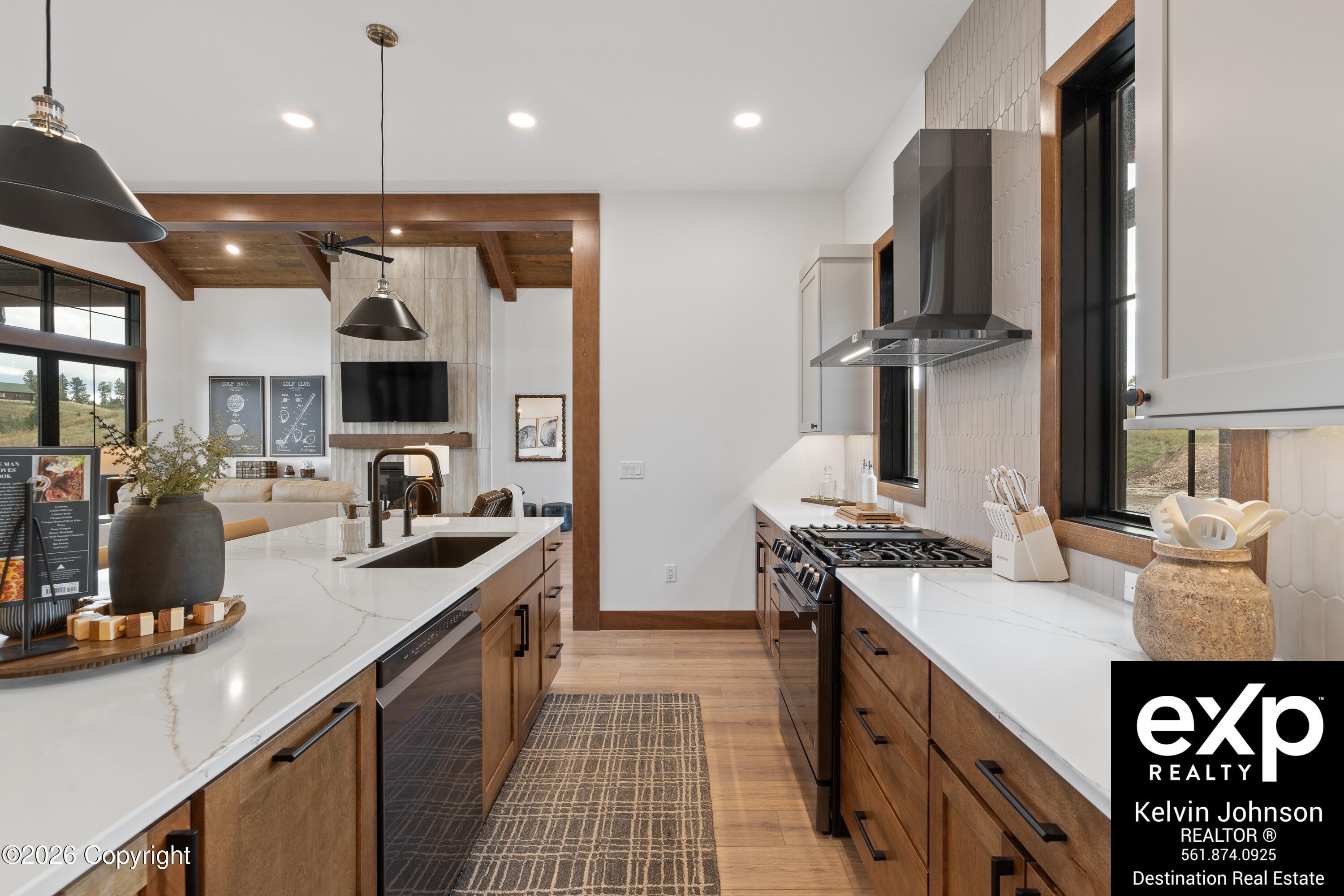 Modern kitchen with a white stone island, warm wood cabinets, gas range, and adjoining living area.
