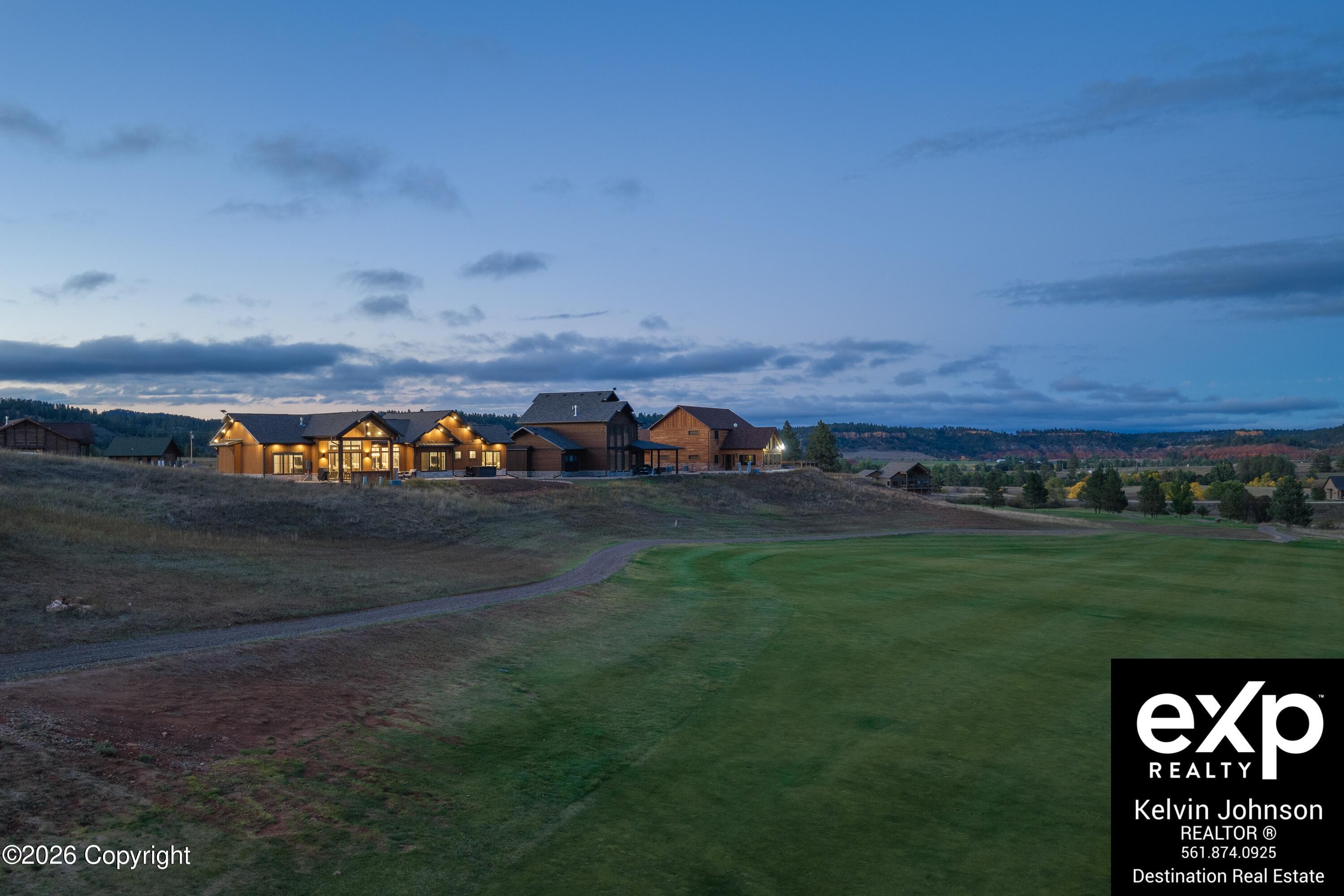 Wood-sided buildings glow beside a golf course green at dusk, with wooded hills in the distance.