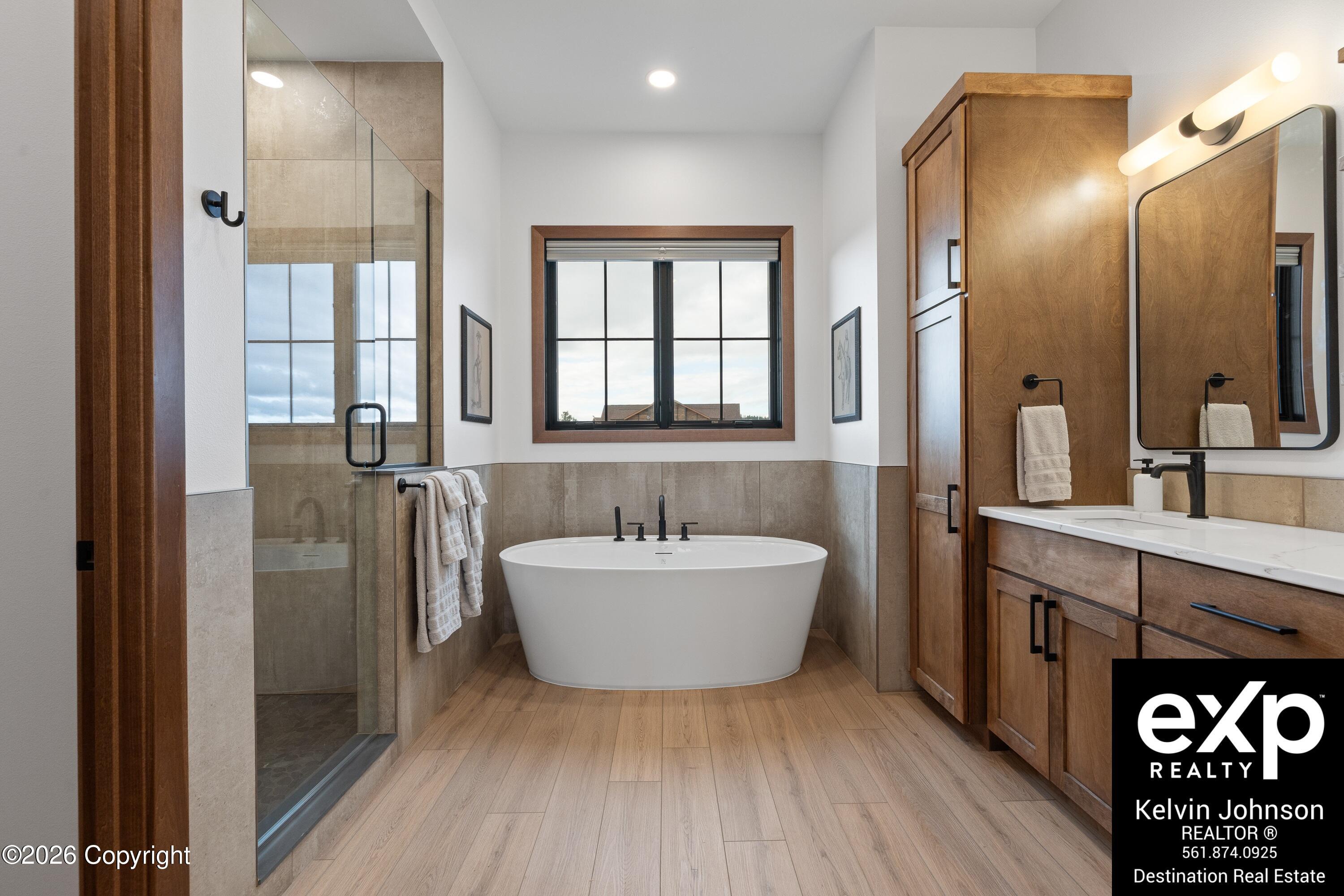 Modern bathroom with a freestanding soaking tub, glass shower, and warm wood cabinetry.