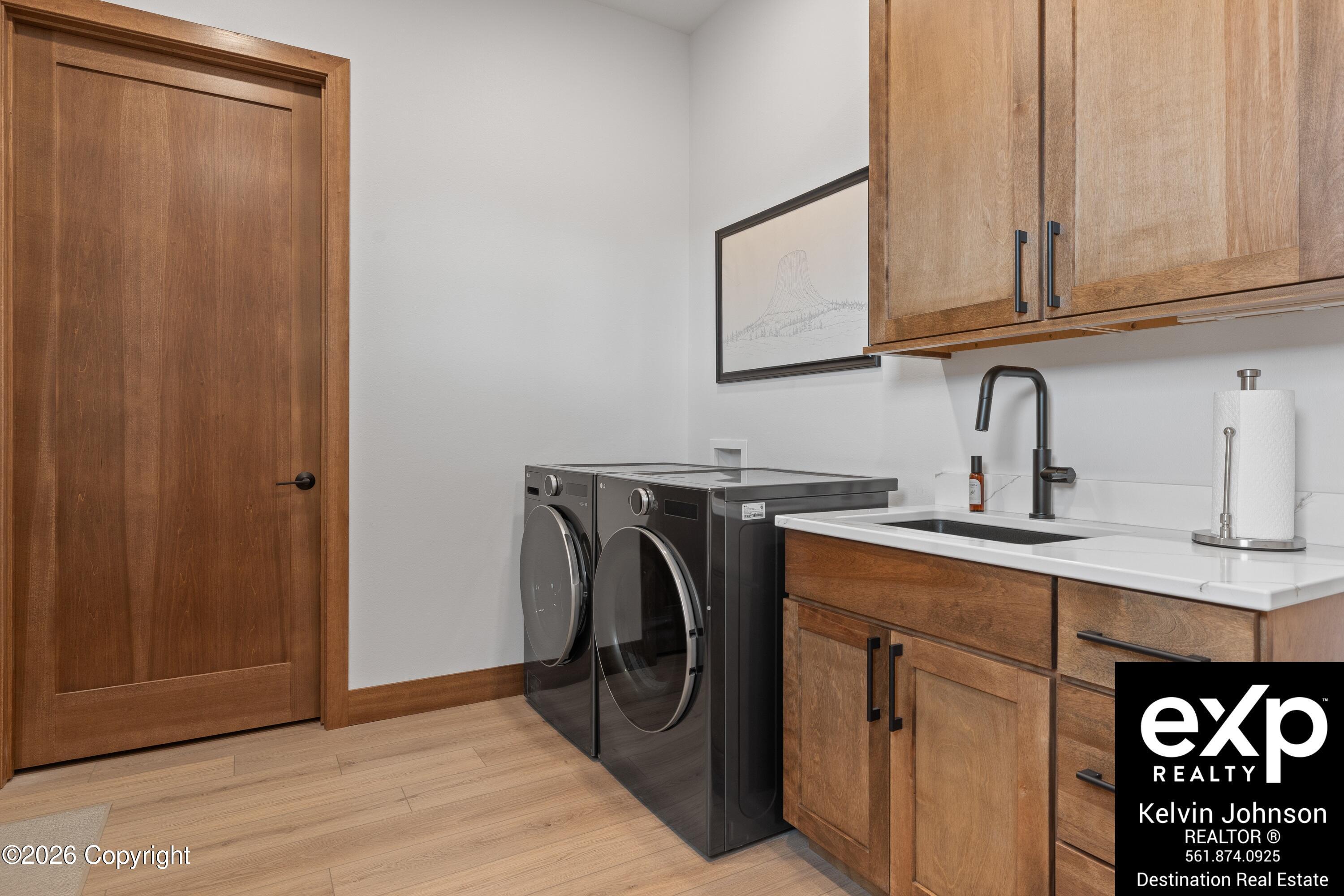 Laundry room with front-loading washer and dryer, wood cabinets, and a sink.
