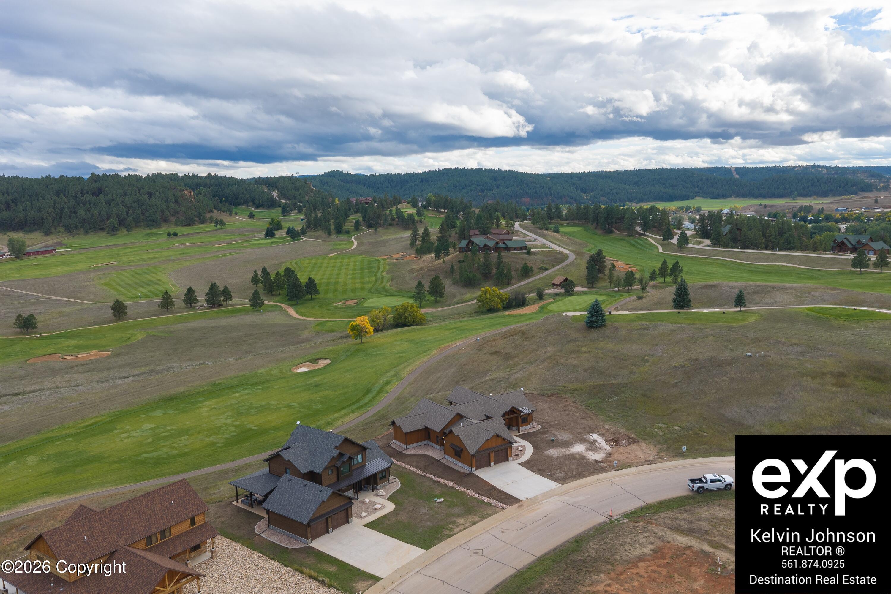 Aerial view of a golf course and wooded hills, with several homes beside a curving road.