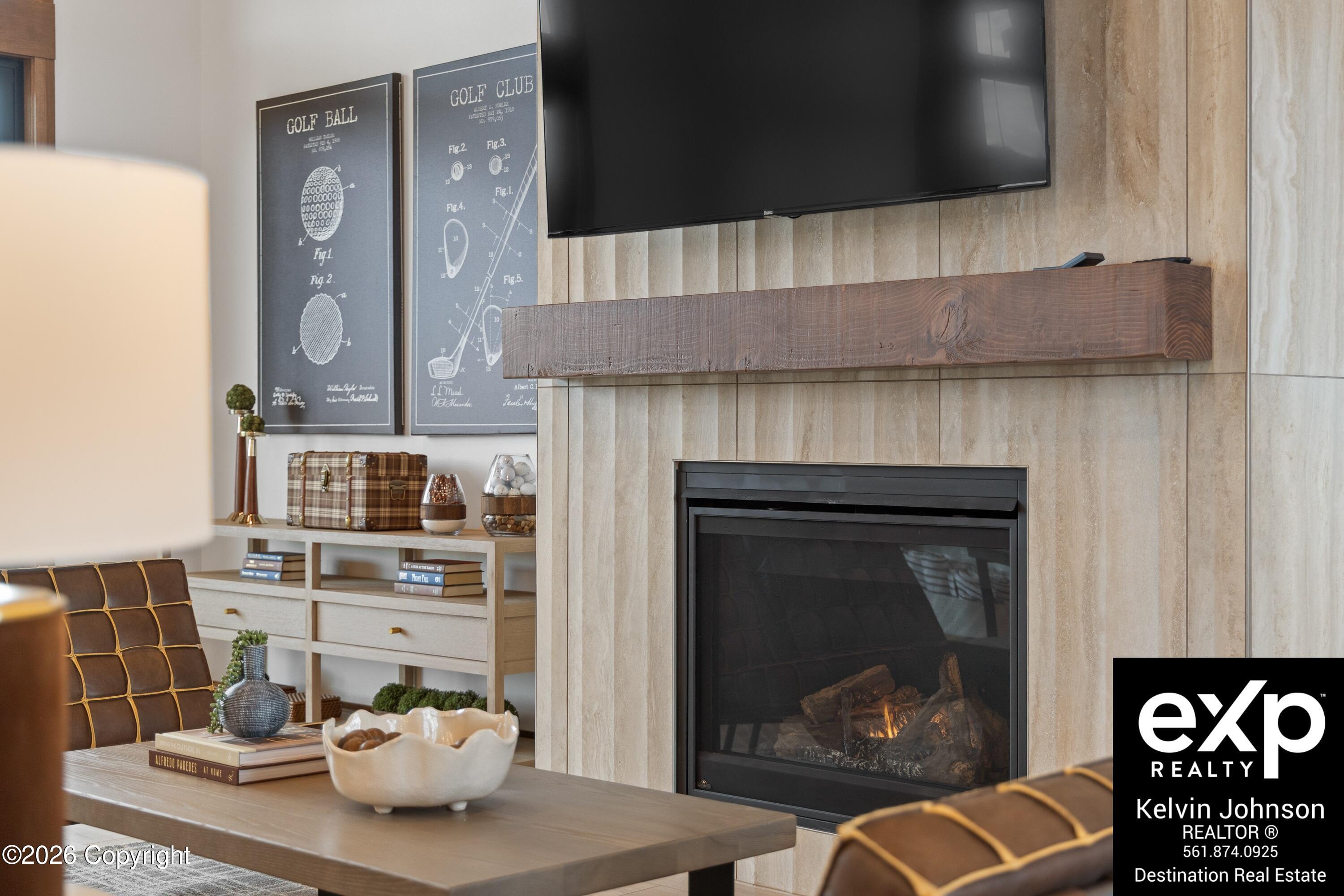 Furnished living room with a stone fireplace, wood mantel, mounted television, and golf-themed wall prints.