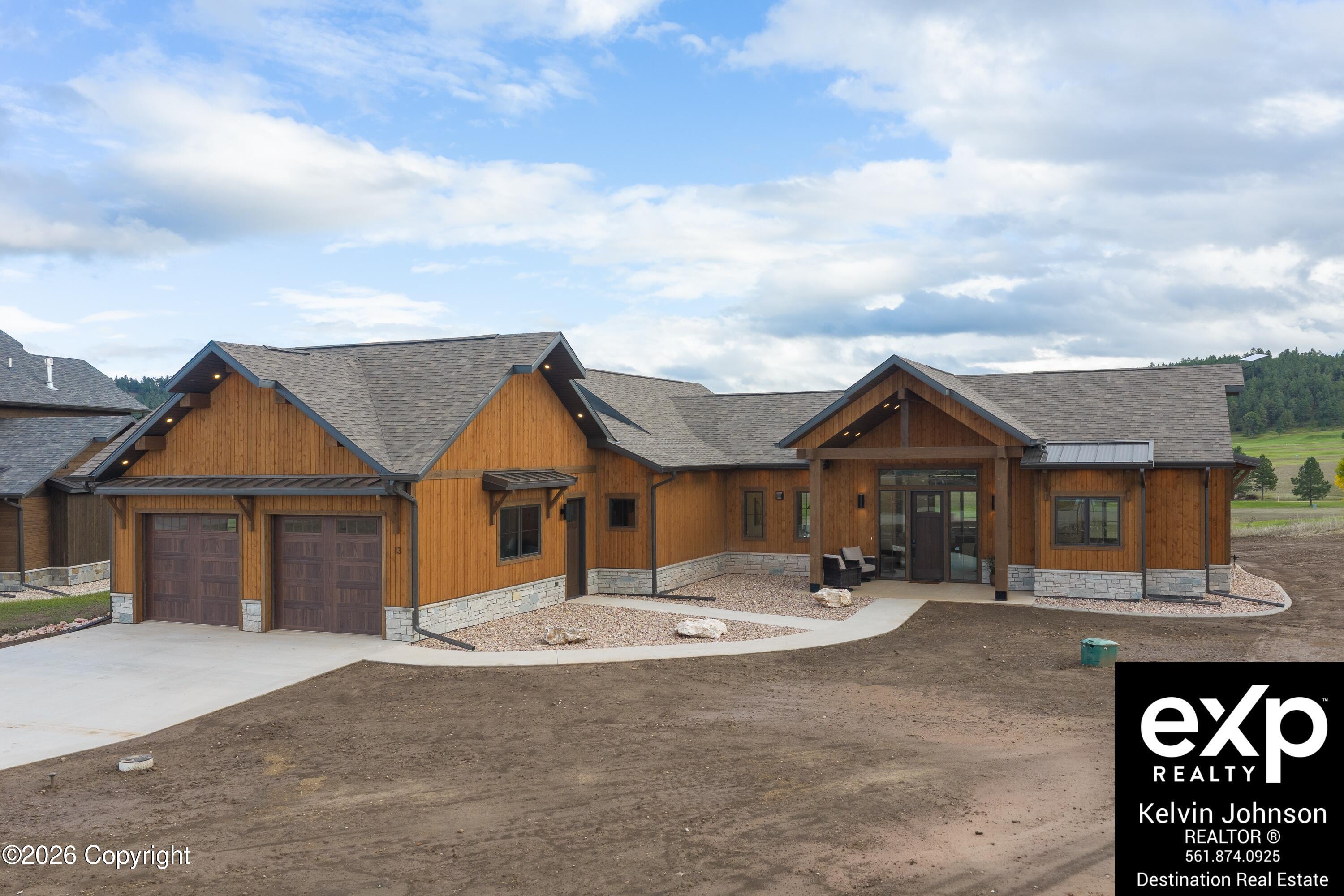 Wood-sided home with a double garage and covered entrance, shown against open grassy land.