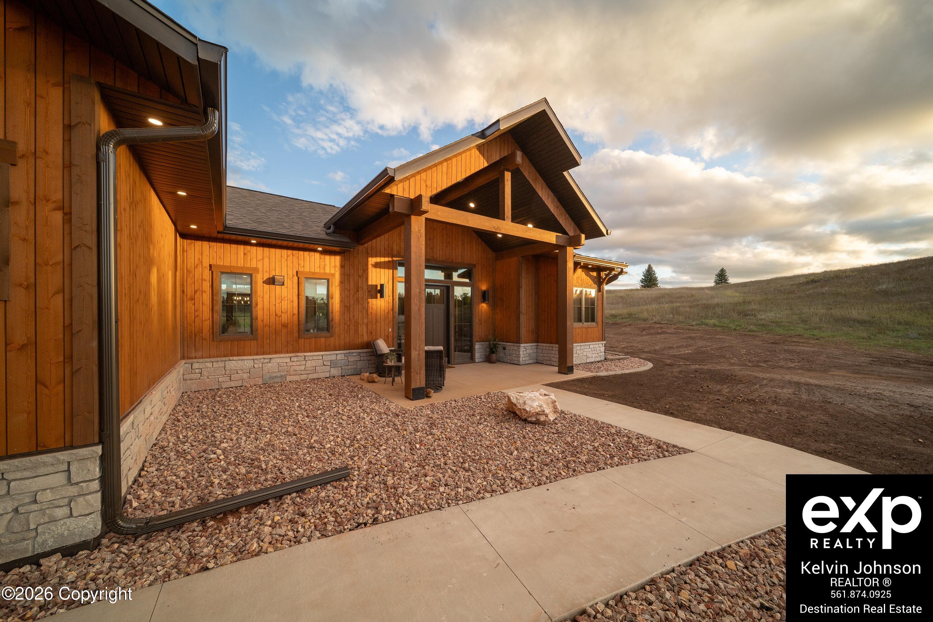 Wood-sided home with a timber-framed covered entry, stone base, gravel landscaping, and open hillside.