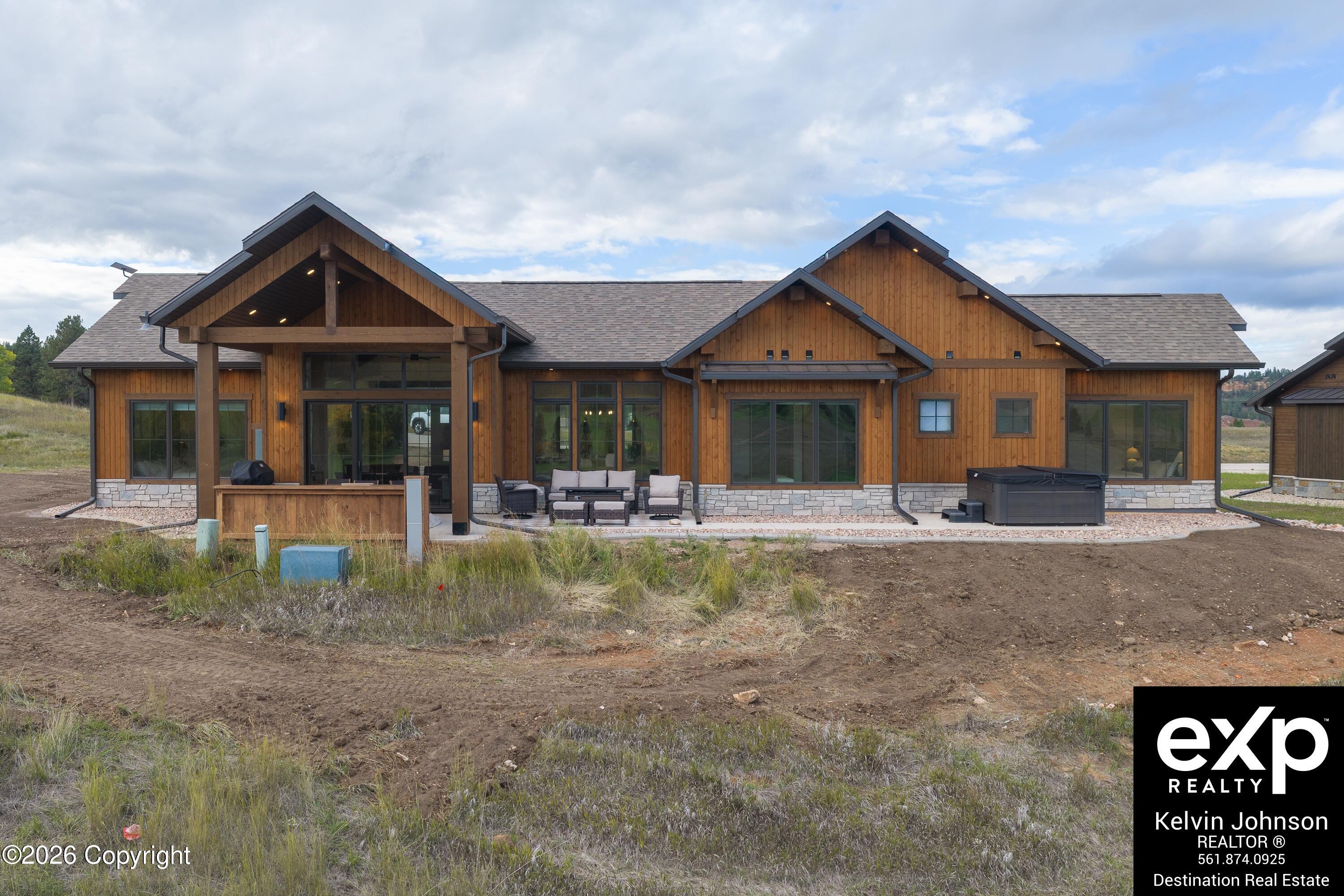 Wood-sided home with a covered patio, outdoor seating, and hot tub at the rear.