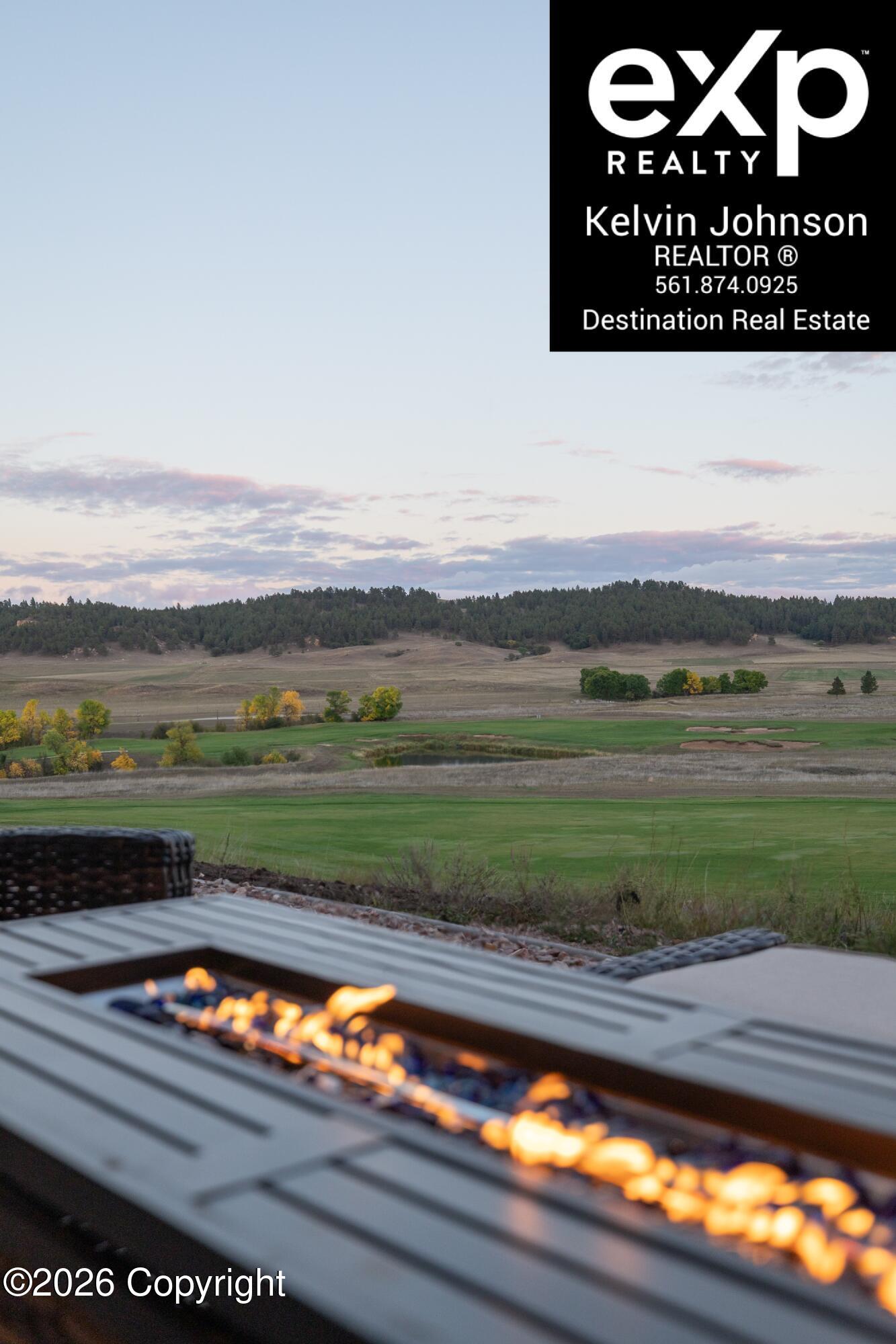 Patio fire table overlooks green fields and wooded hills at dusk.