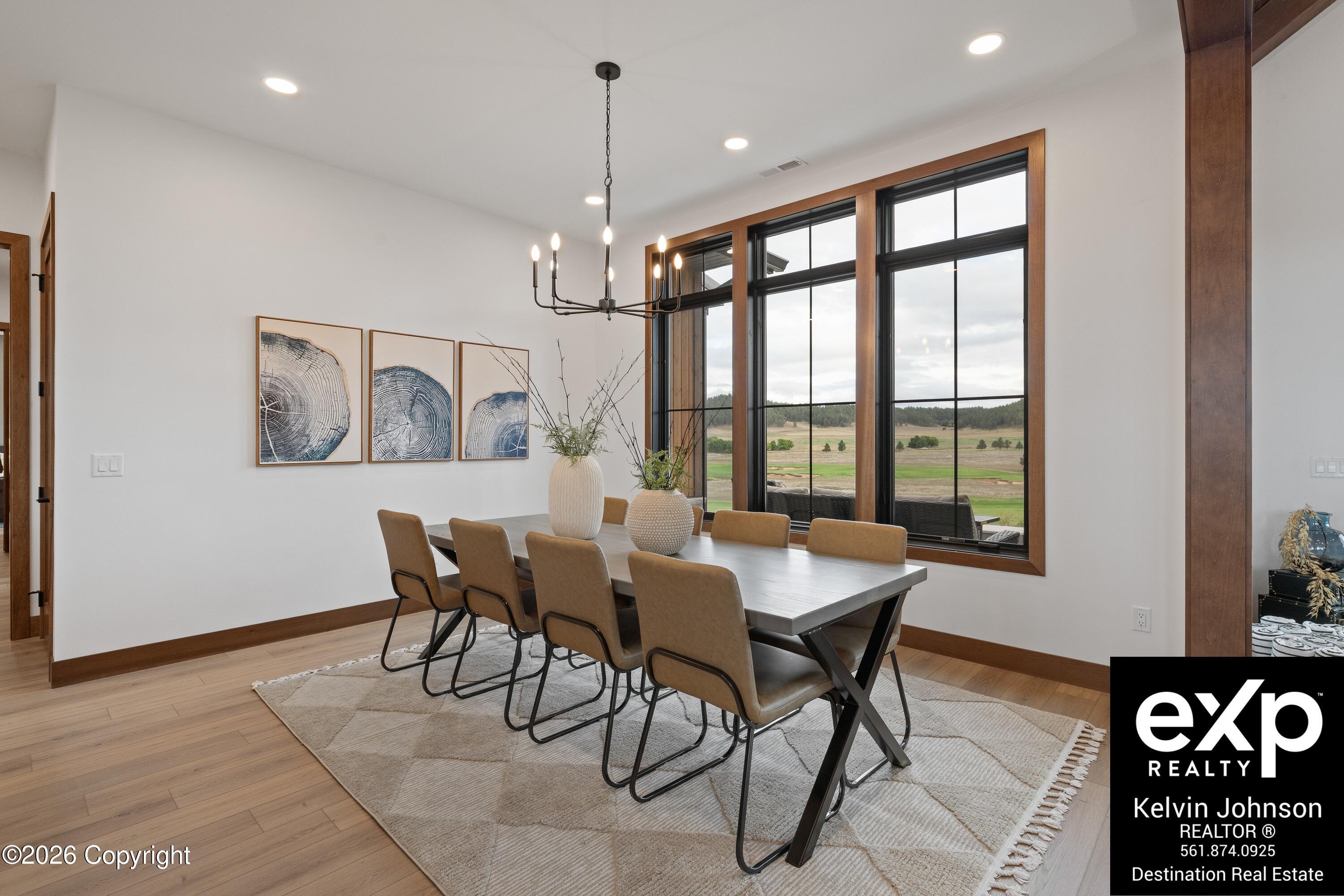 Dining room with a long table, tan chairs, and large windows overlooking open fields.