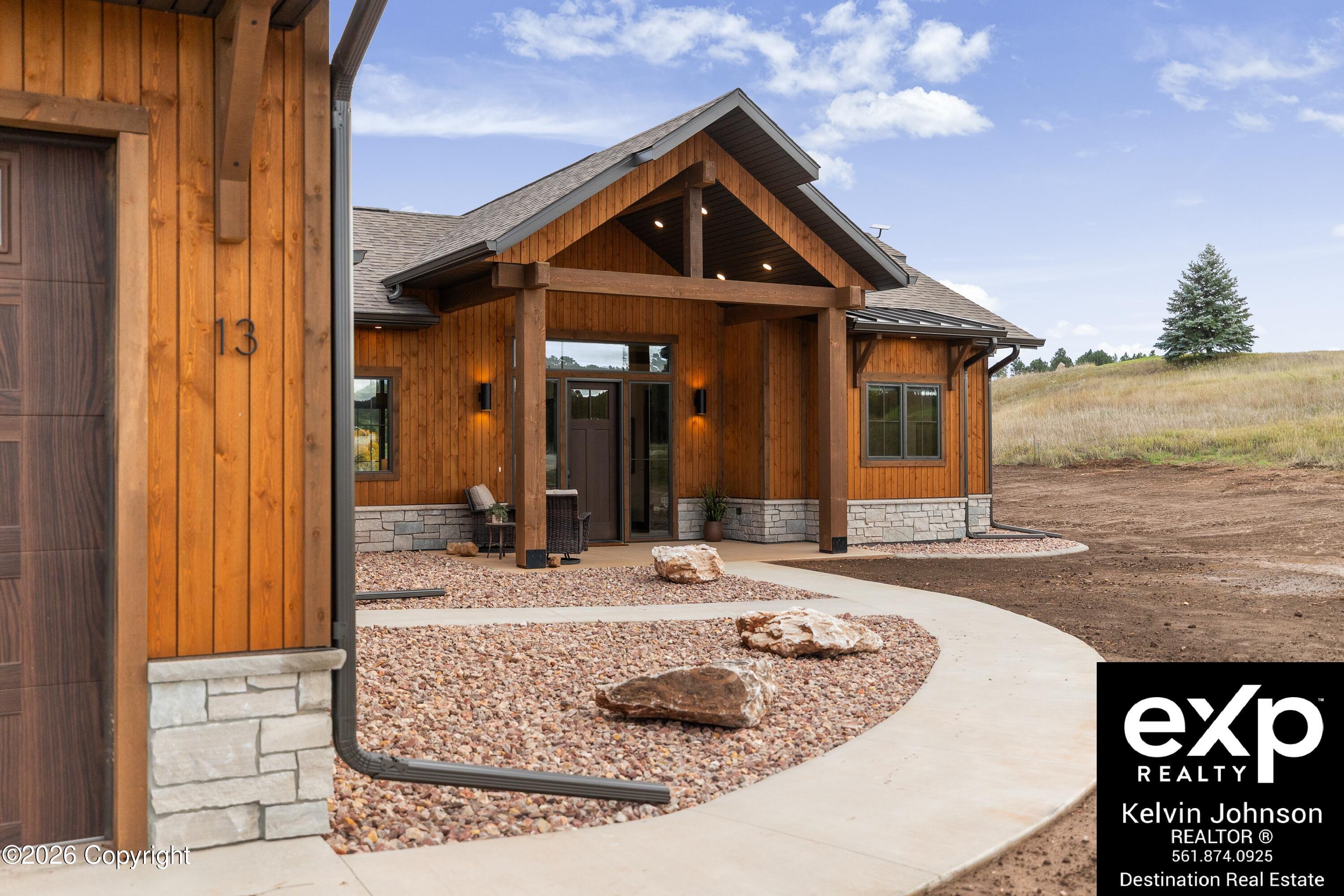 Modern wood-sided home with a timber-framed entry, stone base, and curved walkway through rock landscaping.