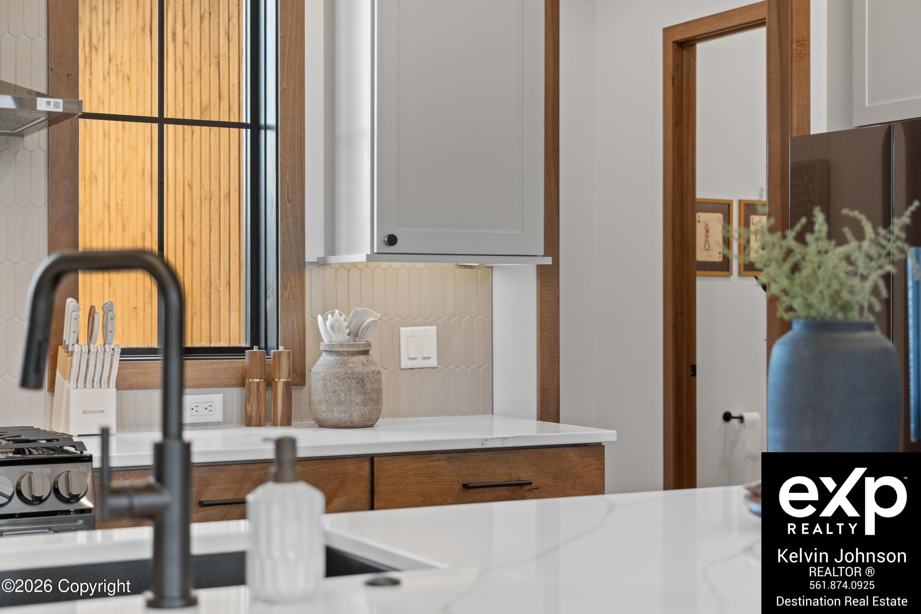 Kitchen with white cabinetry, warm wood drawers, and a large window with wooden blinds.