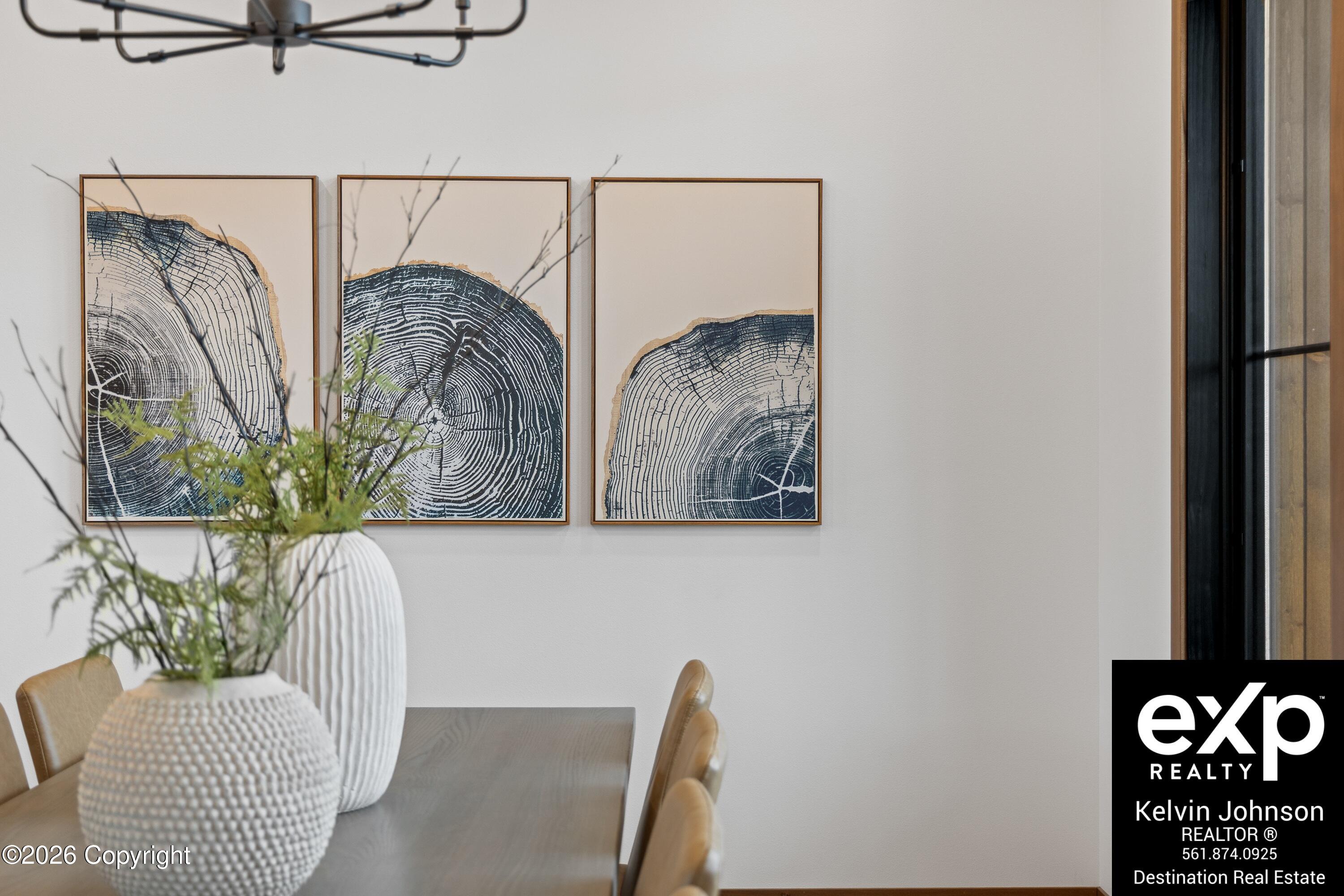 Dining area with a wood table, tan chairs, sculptural vases, and framed tree-ring artwork.