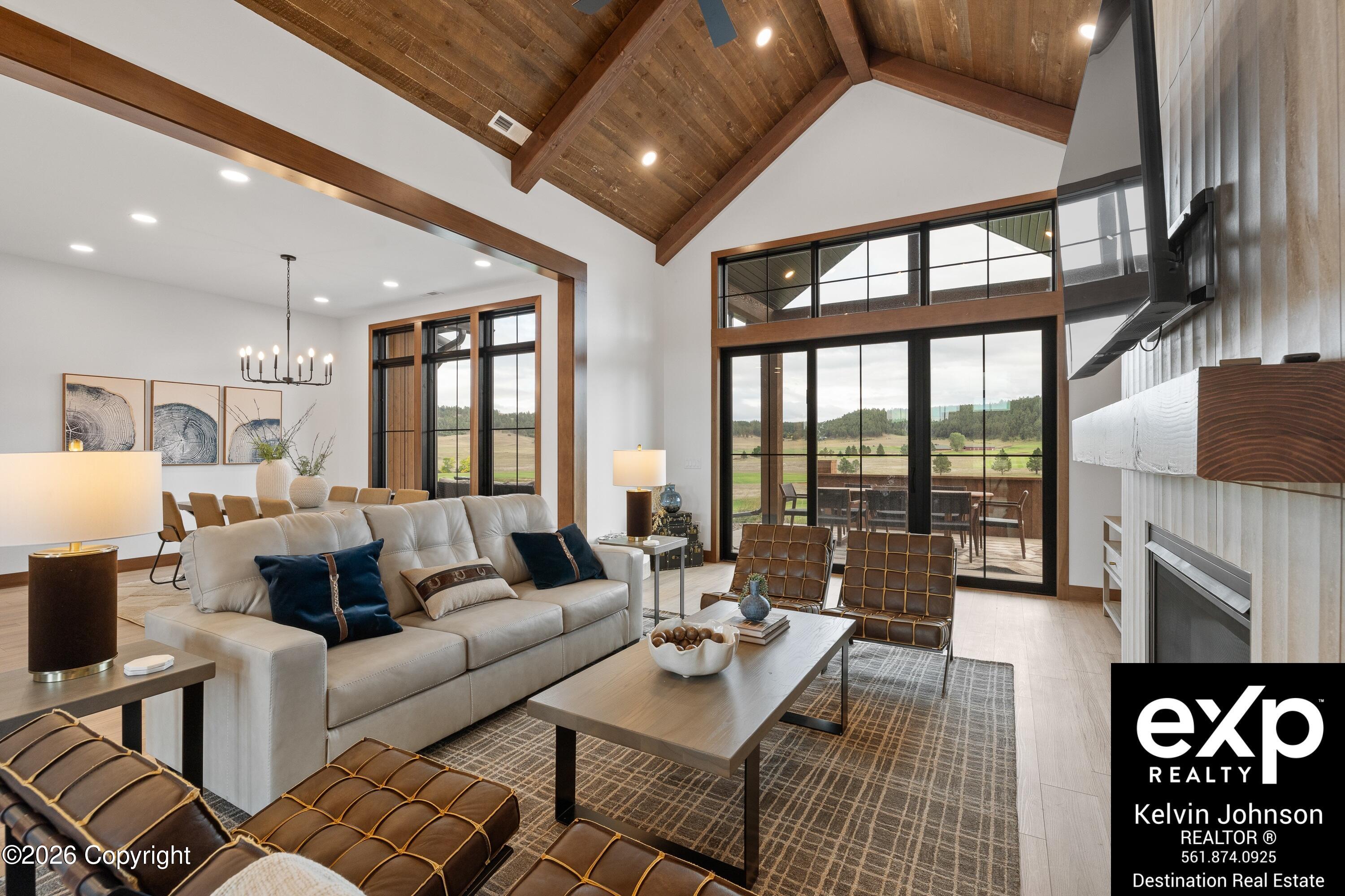 Living room with a vaulted wood ceiling, large windows, a fireplace, and views of open fields.