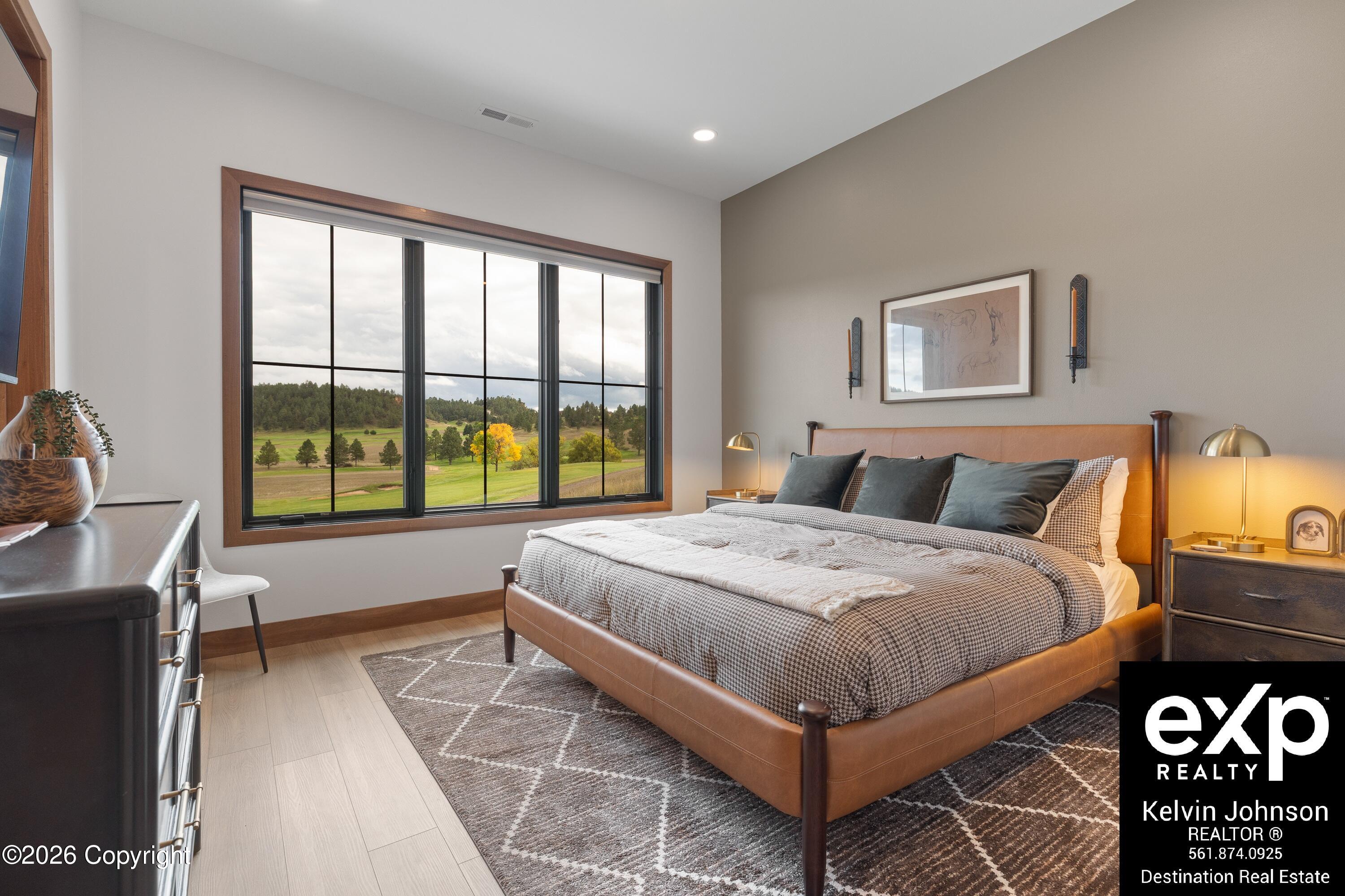Bedroom with a brown upholstered bed and a large window overlooking fields and autumn trees.