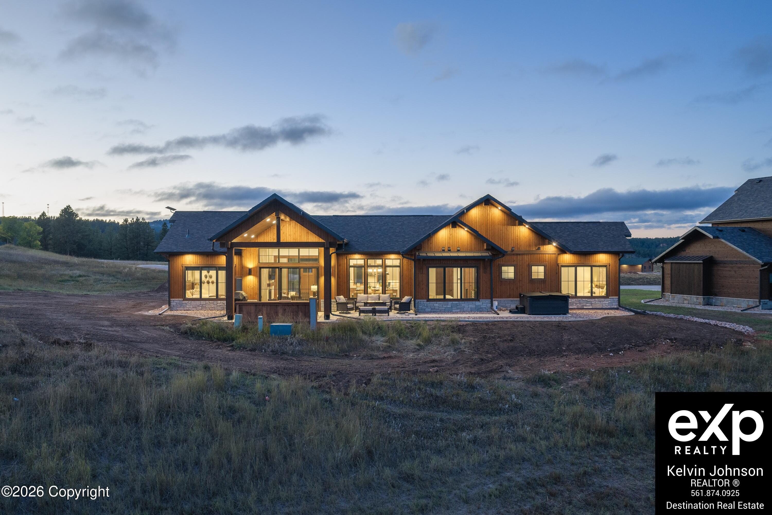 Modern wood-sided home glowing at dusk, with multiple gables and a patio seating area.