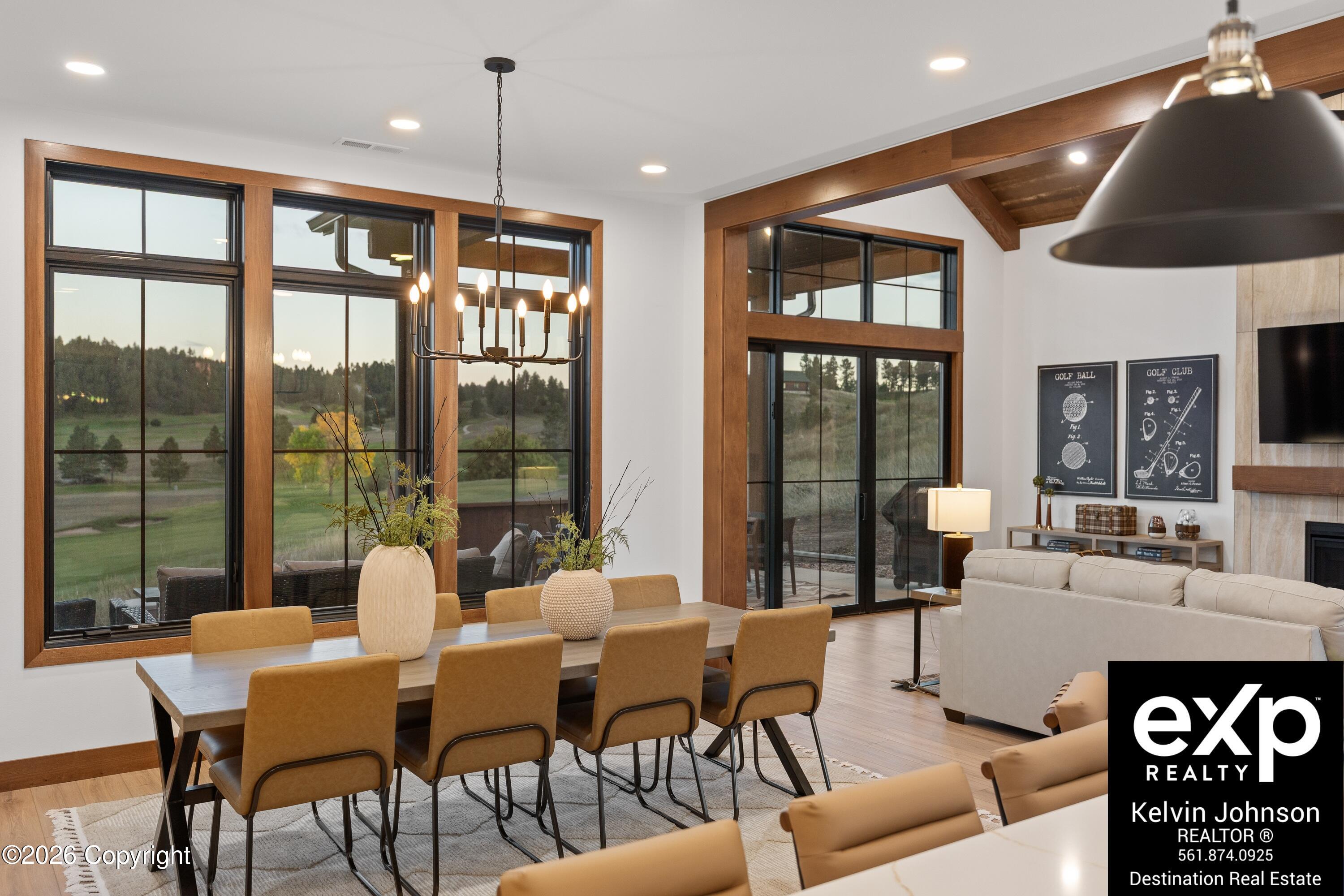 Dining and living area with wood-trimmed windows overlooking a golf course and a long table beneath a chandelier.