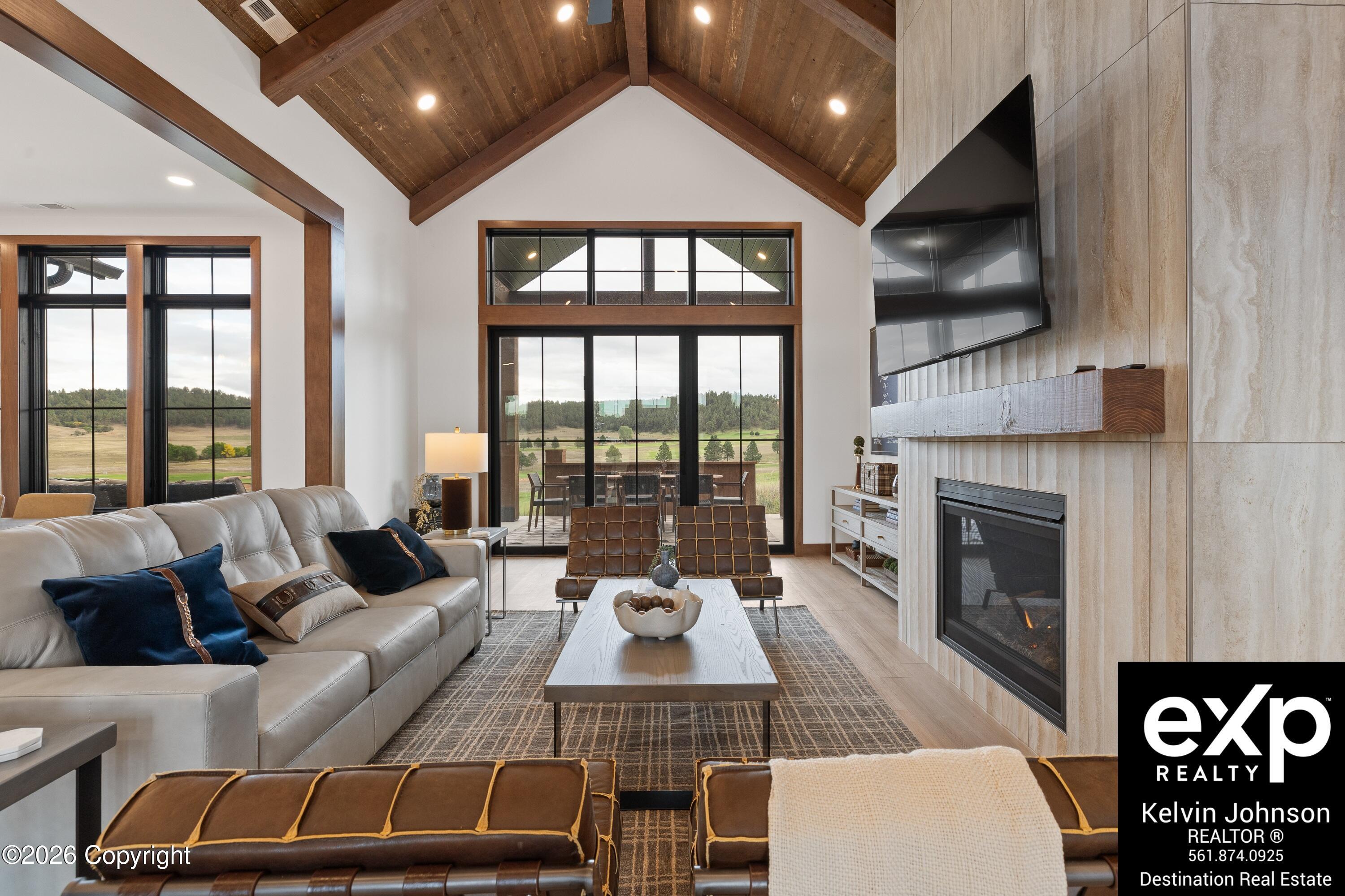Living room with a vaulted wood ceiling, stone fireplace, and large windows overlooking open countryside.