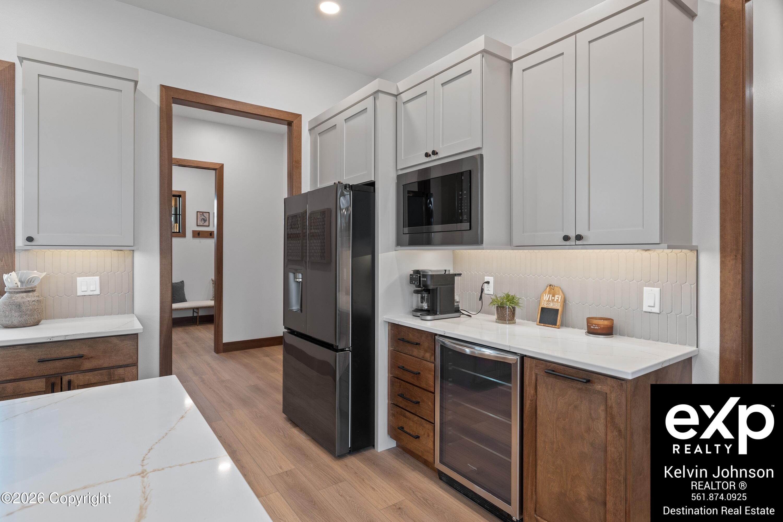 Kitchen with white cabinets, warm wood accents, black appliances, and a coffee station.