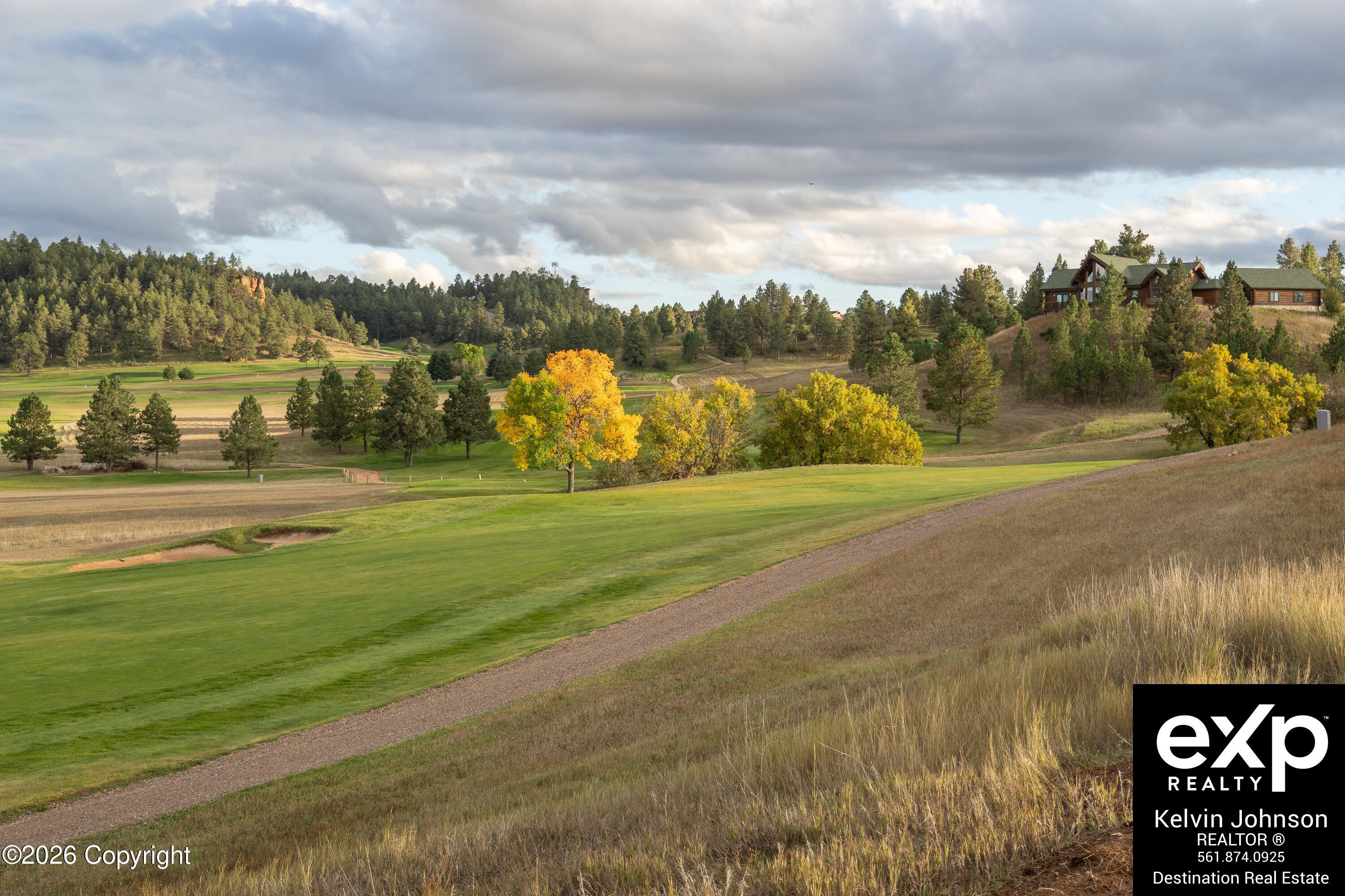 Golf course and gravel path with autumn trees and a log home on a wooded rise.