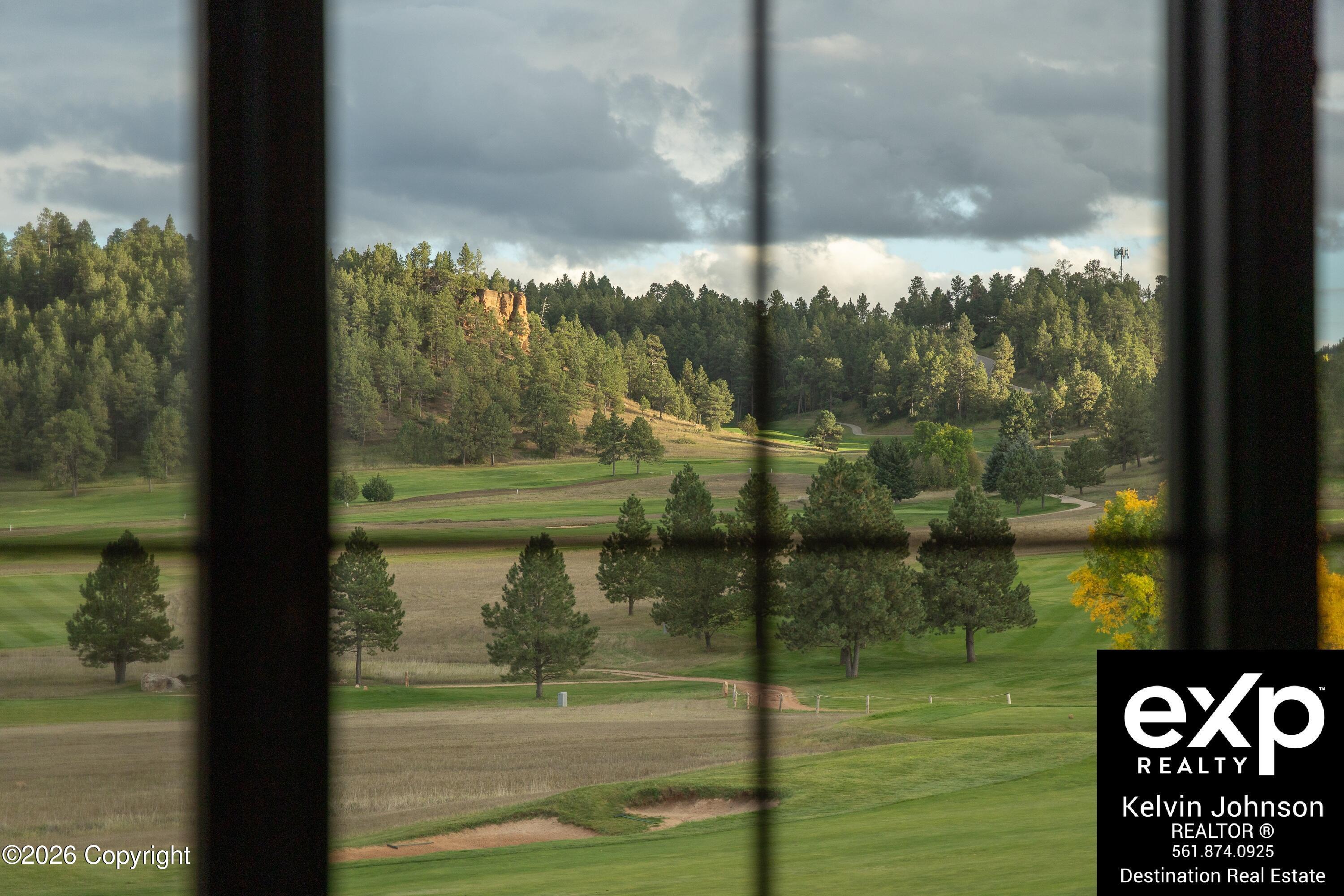 Golf course and wooded hills viewed through dark window bars.