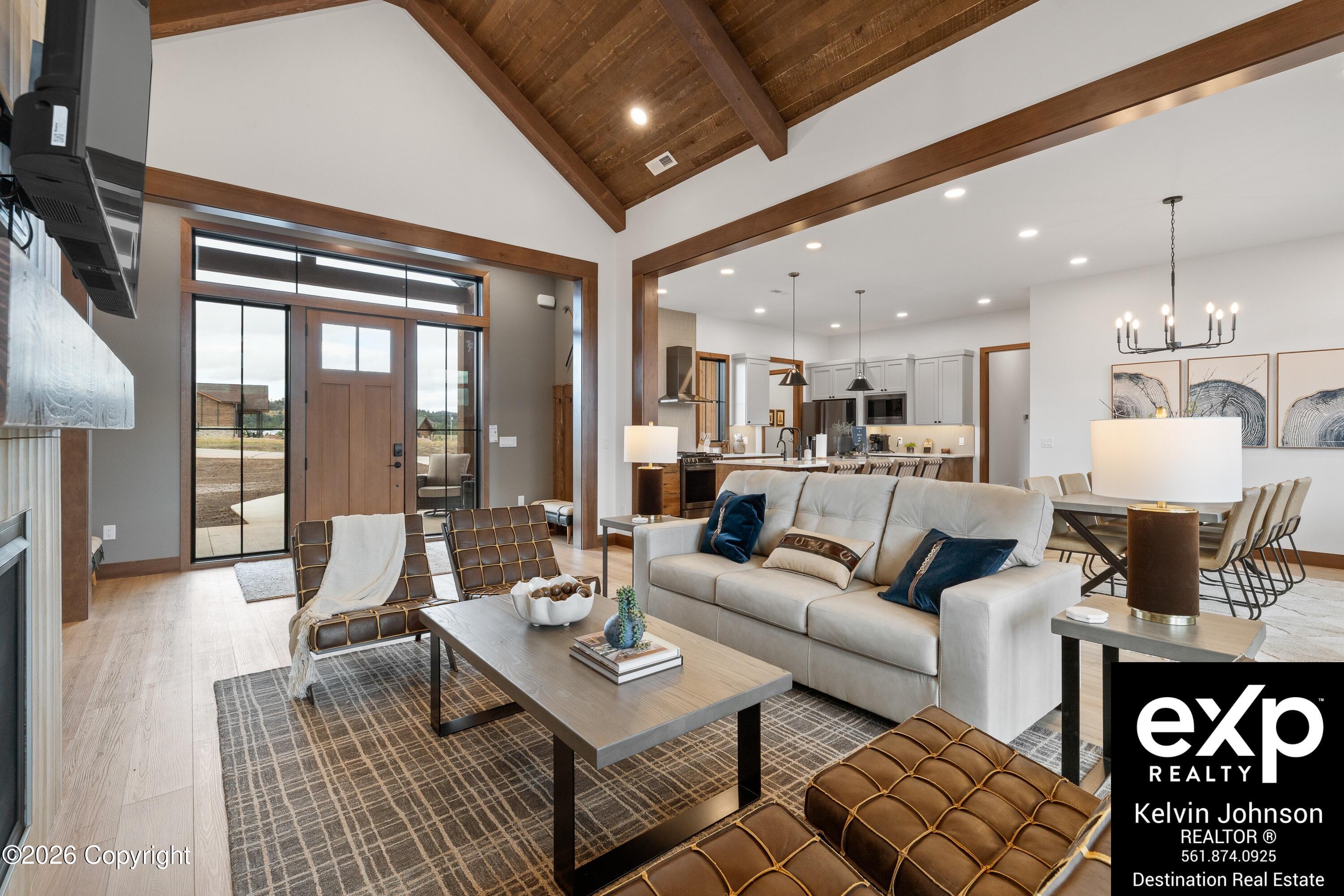 Open-plan living room and kitchen beneath a vaulted wood ceiling, with a tall glazed entry and furnished seating.