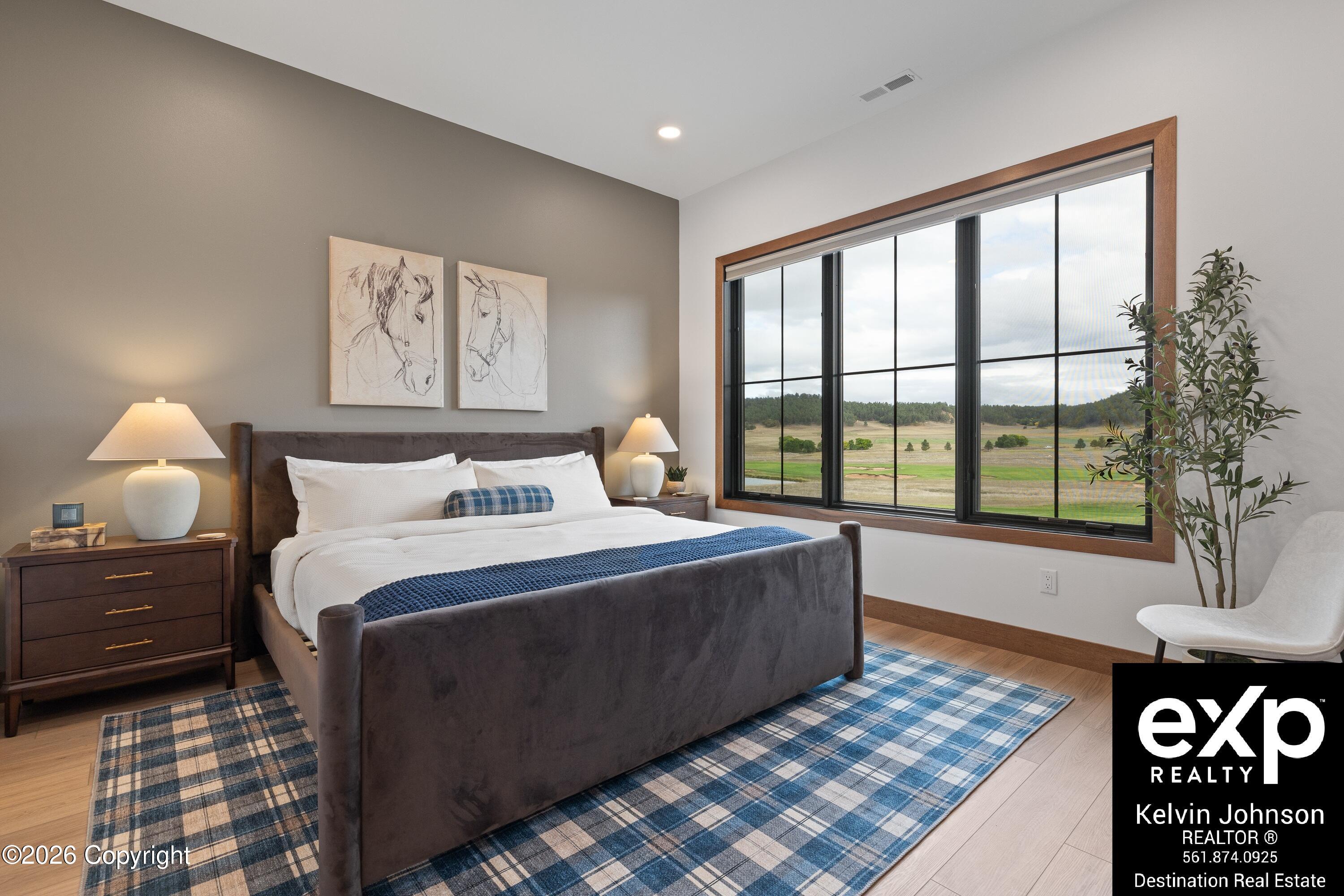 Bedroom with a gray upholstered bed and large window overlooking open fields.