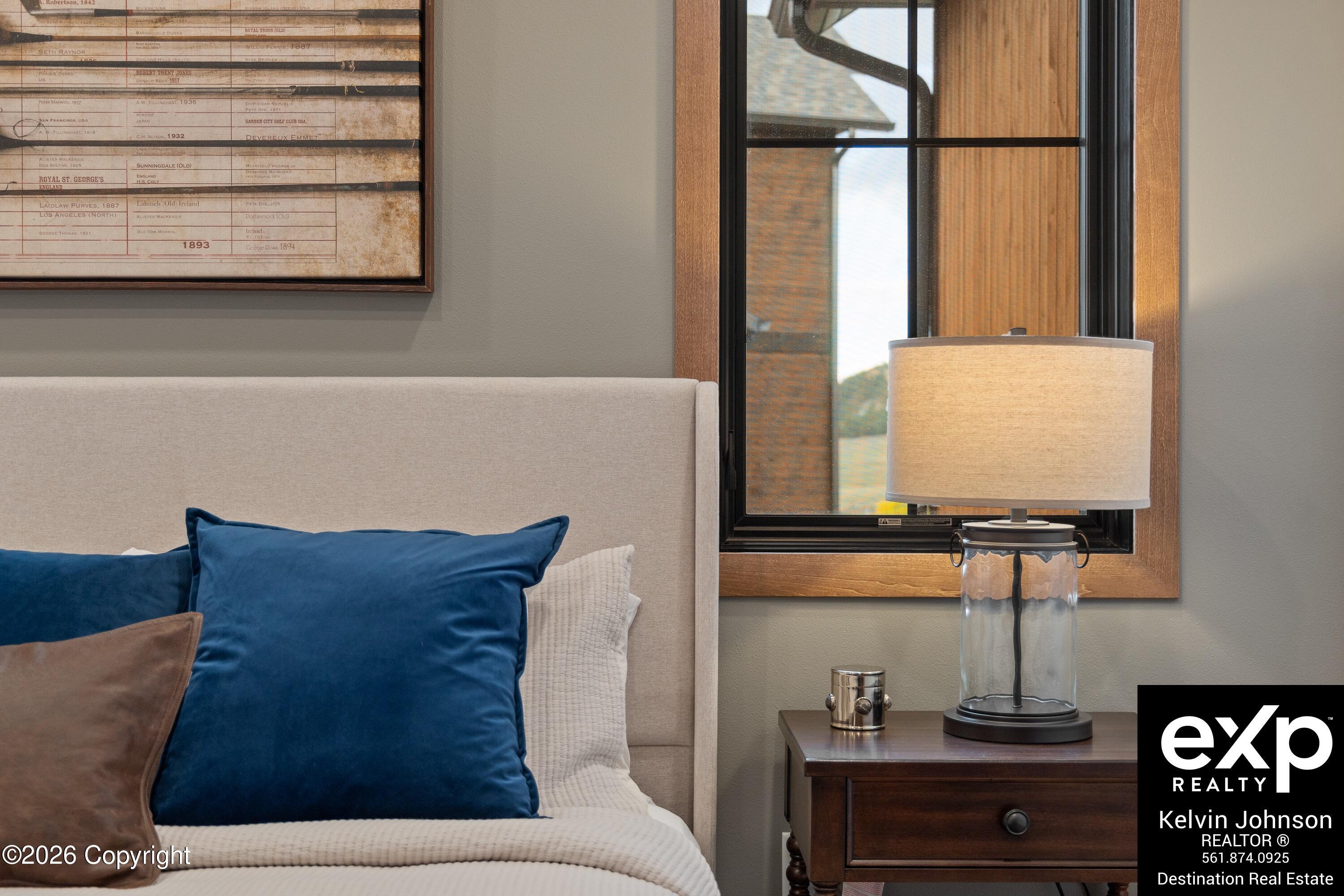 Furnished bedroom with navy pillows, a glass-based bedside lamp, and a wood-trimmed window.