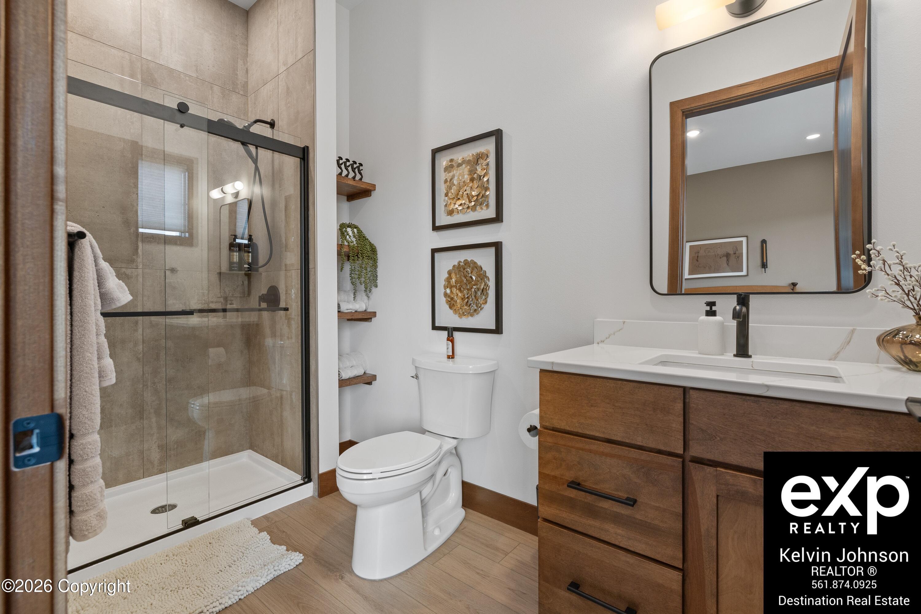 Modern bathroom with beige-tiled glass shower, wood vanity, and large rounded-corner mirror.