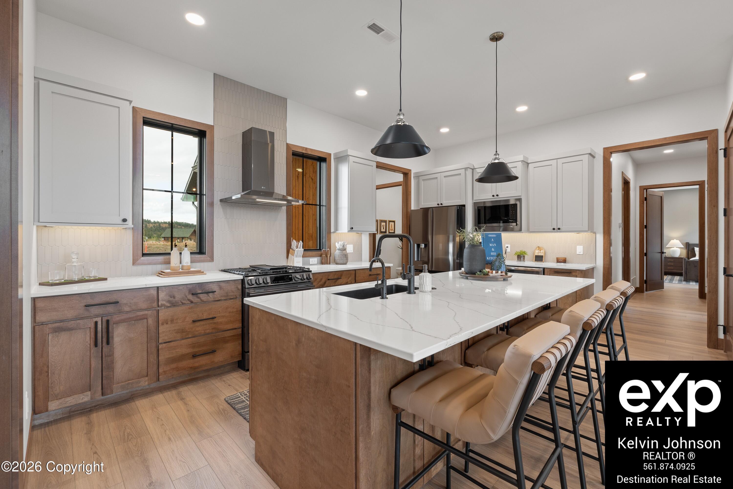 Modern kitchen with a large white island, wood cabinetry, stainless steel appliances, and upholstered bar stools.
