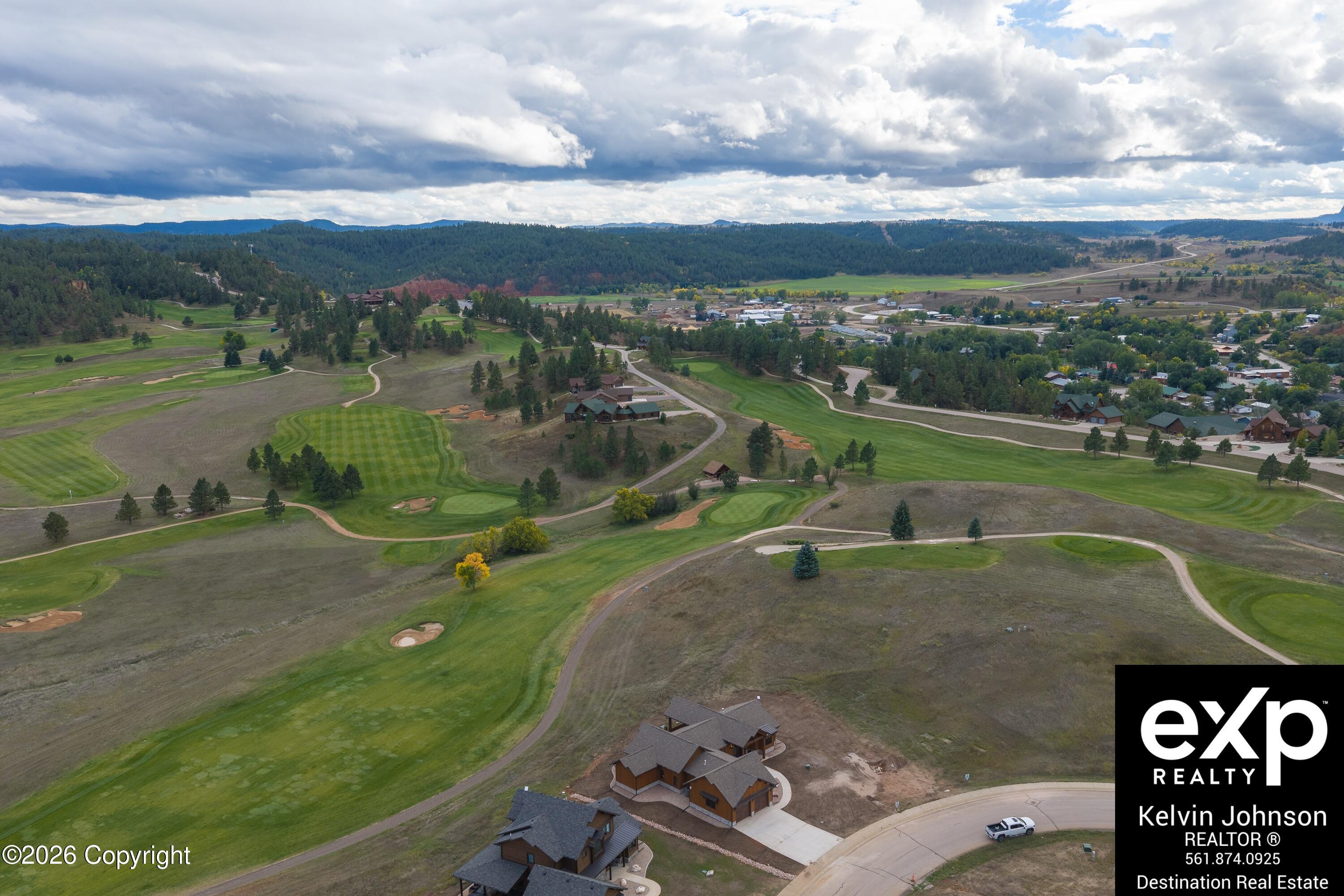 Aerial view of homes beside a golf course, with winding paths and wooded hills.