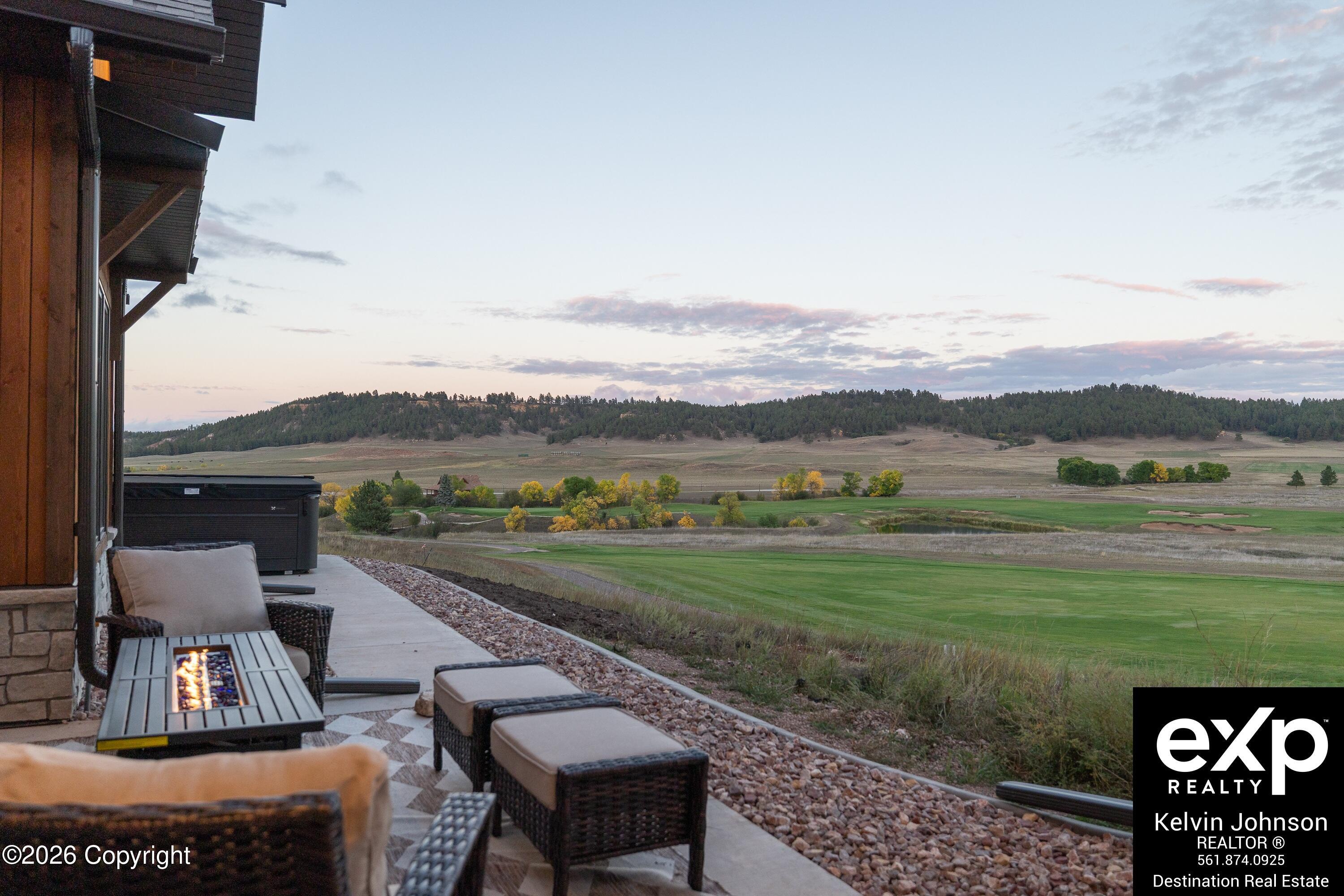 Furnished patio with a fire table overlooks a golf course and wooded hills at dusk.