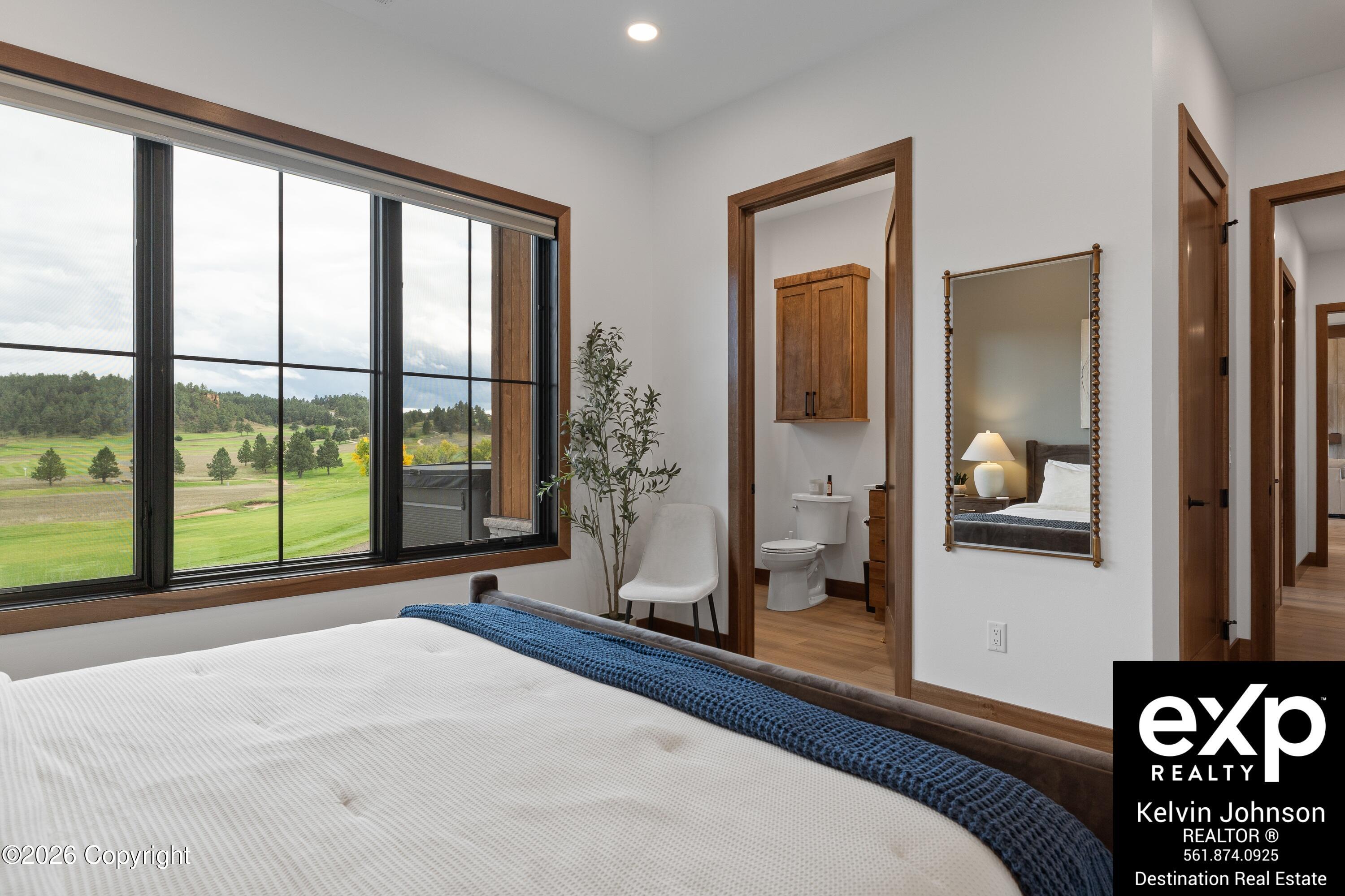 Bedroom with a blue throw, large picture window, and views of green grounds and wooded hills.