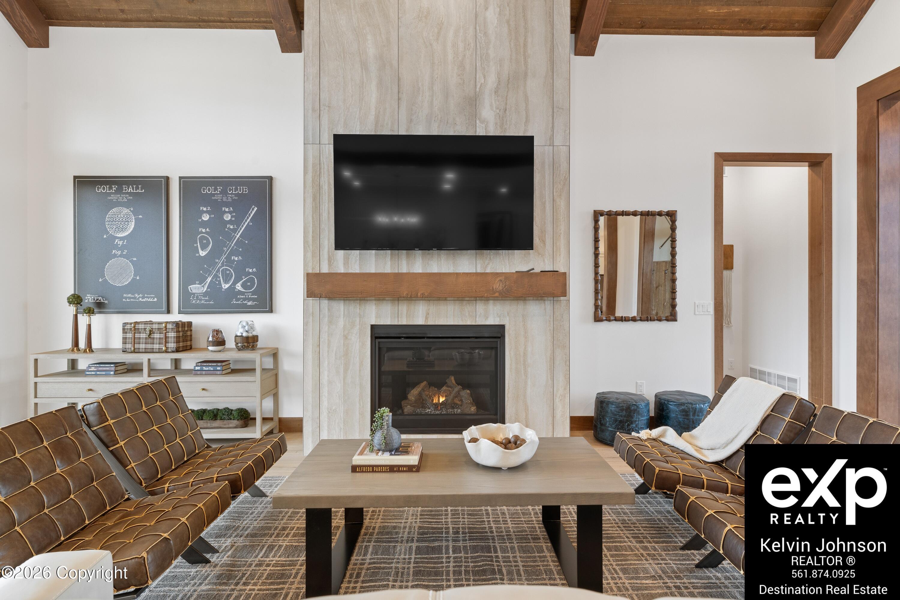 Living room with stone fireplace, mounted TV, exposed wood beams, and brown leather seating.