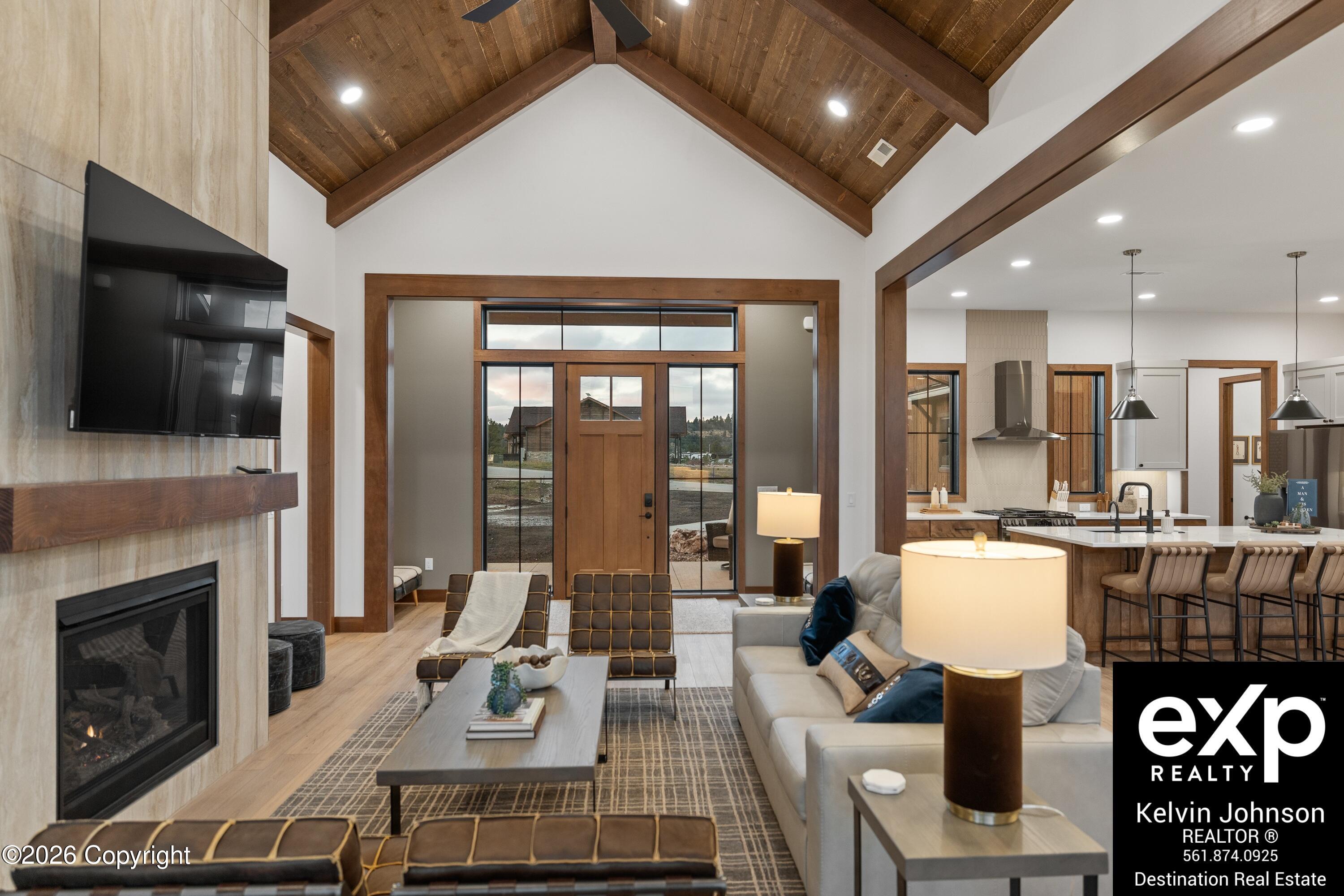 Vaulted living room with exposed wood beams, a stone fireplace, and an open kitchen beyond.