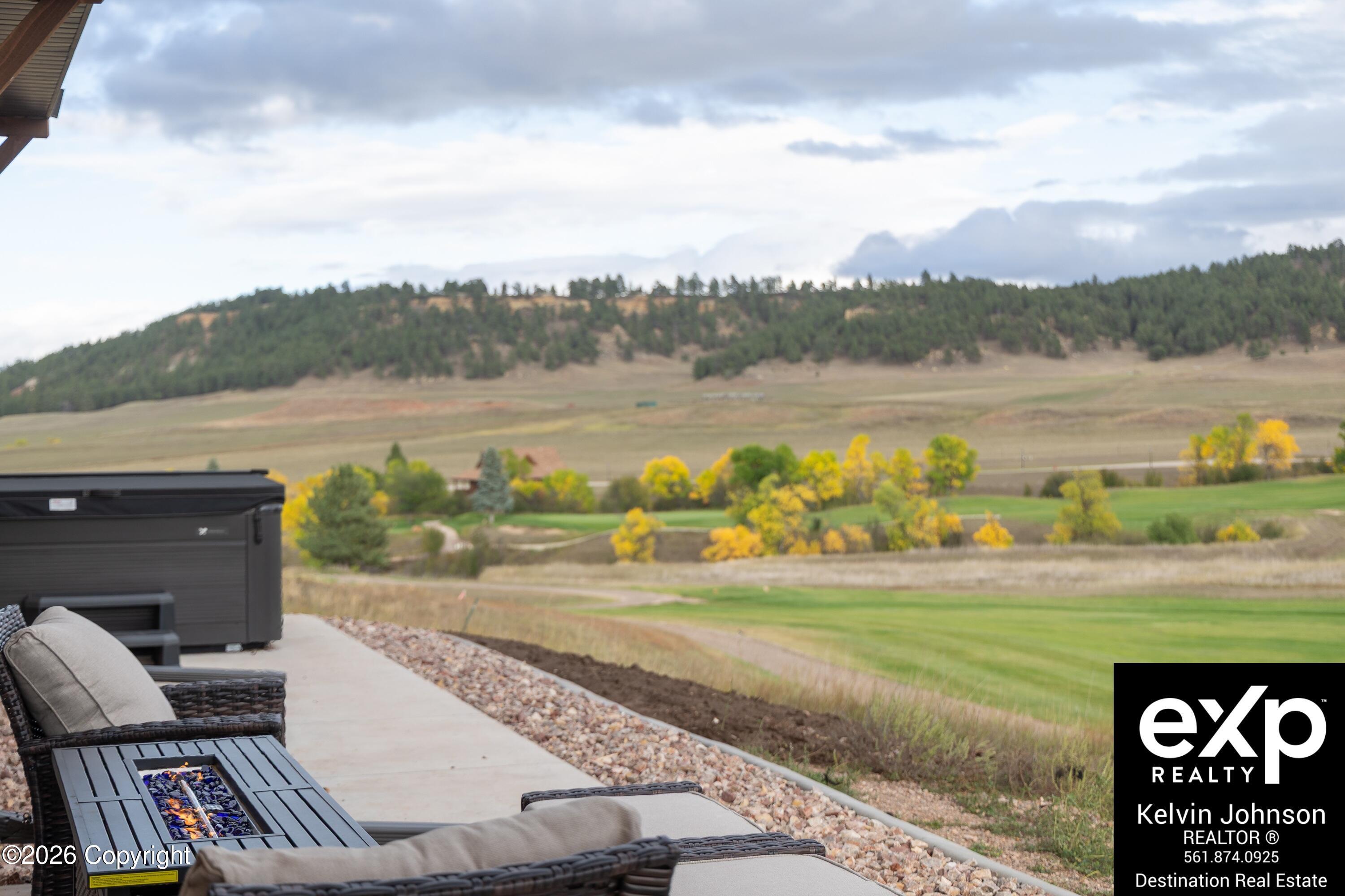 Furnished patio with a fire table and hot tub overlooking a green fairway and autumn-colored trees.