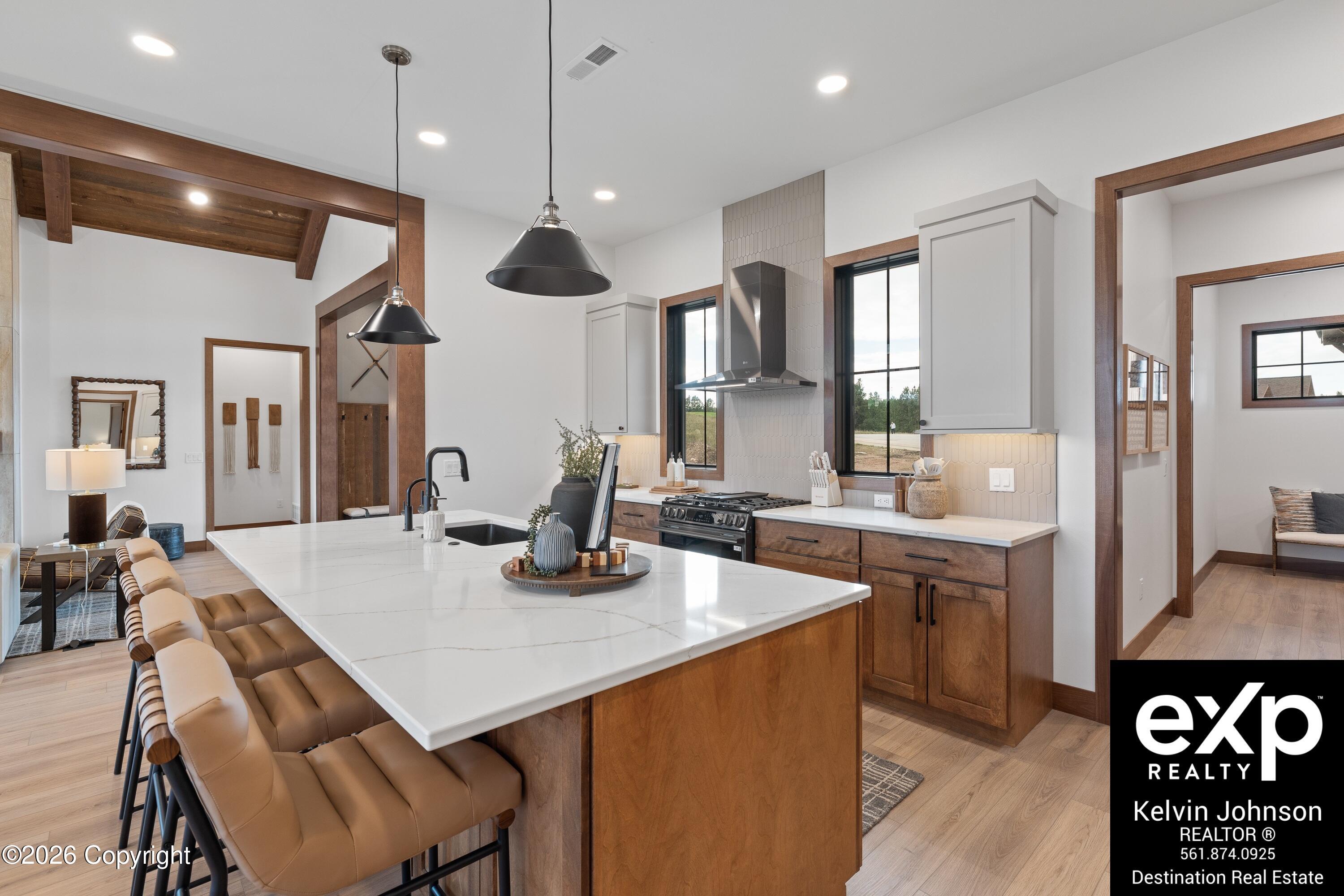 Kitchen with a large white island, tan bar stools, warm wood cabinets, and black pendant lights.